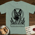 Holy Orders Belgian Malinois T-Shirt flat lay in Bay, featuring a bold black-and-white linocut saint-medallion portrait of a Belgian Malinois.