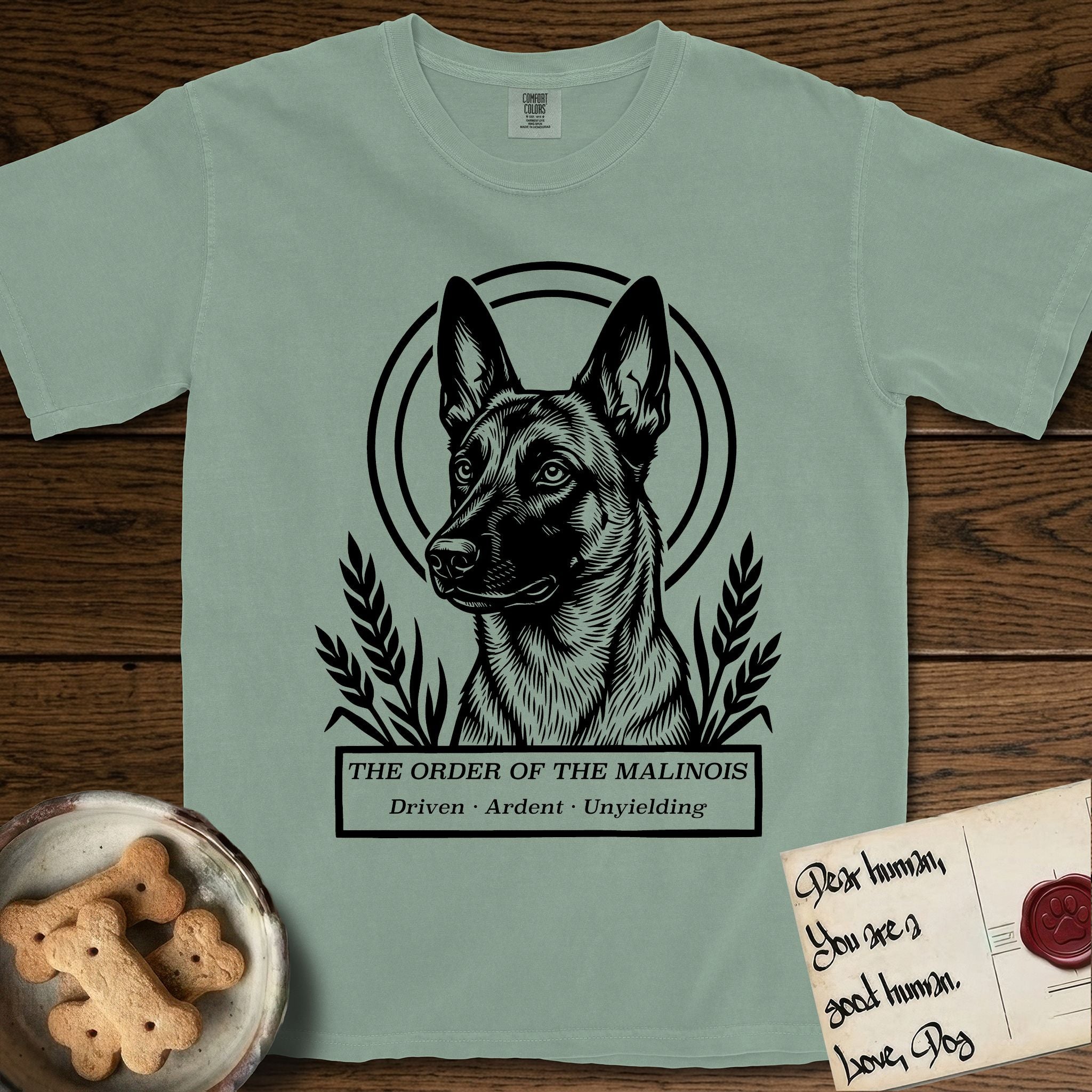 Holy Orders Belgian Malinois T-Shirt flat lay in Bay, featuring a bold black-and-white linocut saint-medallion portrait of a Belgian Malinois.
