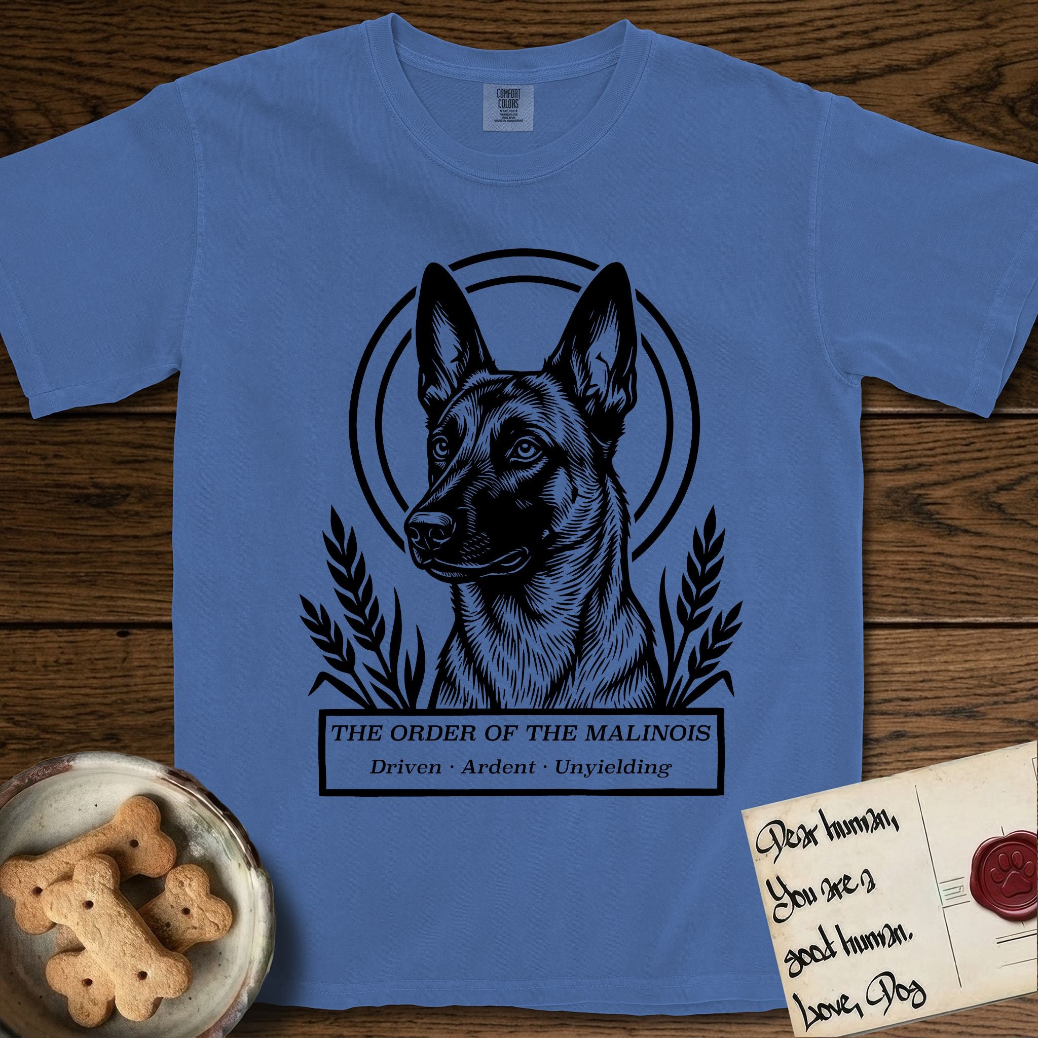 Holy Orders Belgian Malinois T-Shirt flat lay in Mystic Blue, featuring a bold black-and-white linocut saint-medallion portrait of a Belgian Malinois.