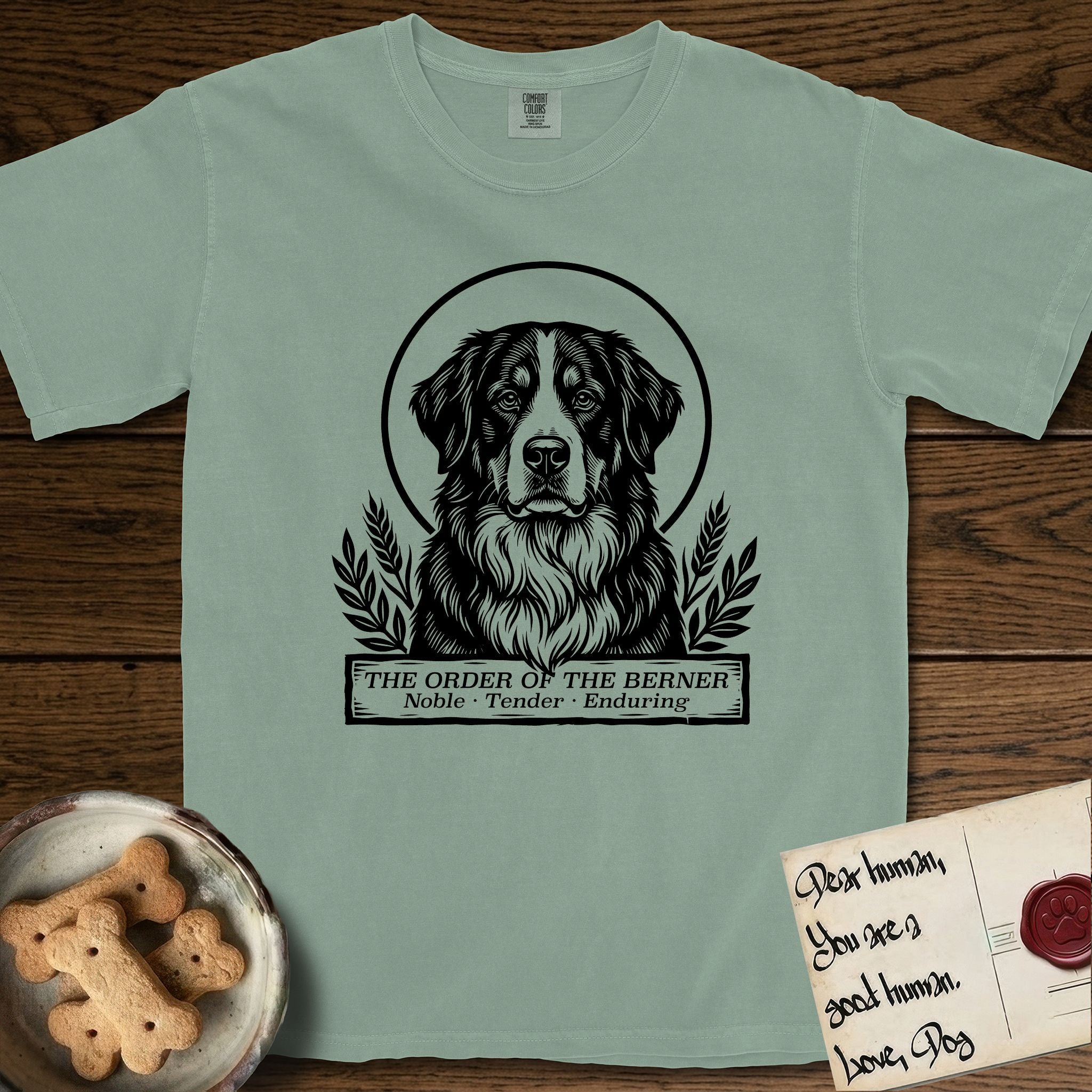 Holy Orders Bernese Mountain Dog T-Shirt flat lay in Bay, featuring a bold black-and-white linocut saint-medallion portrait of a Bernese Mountain Dog.
