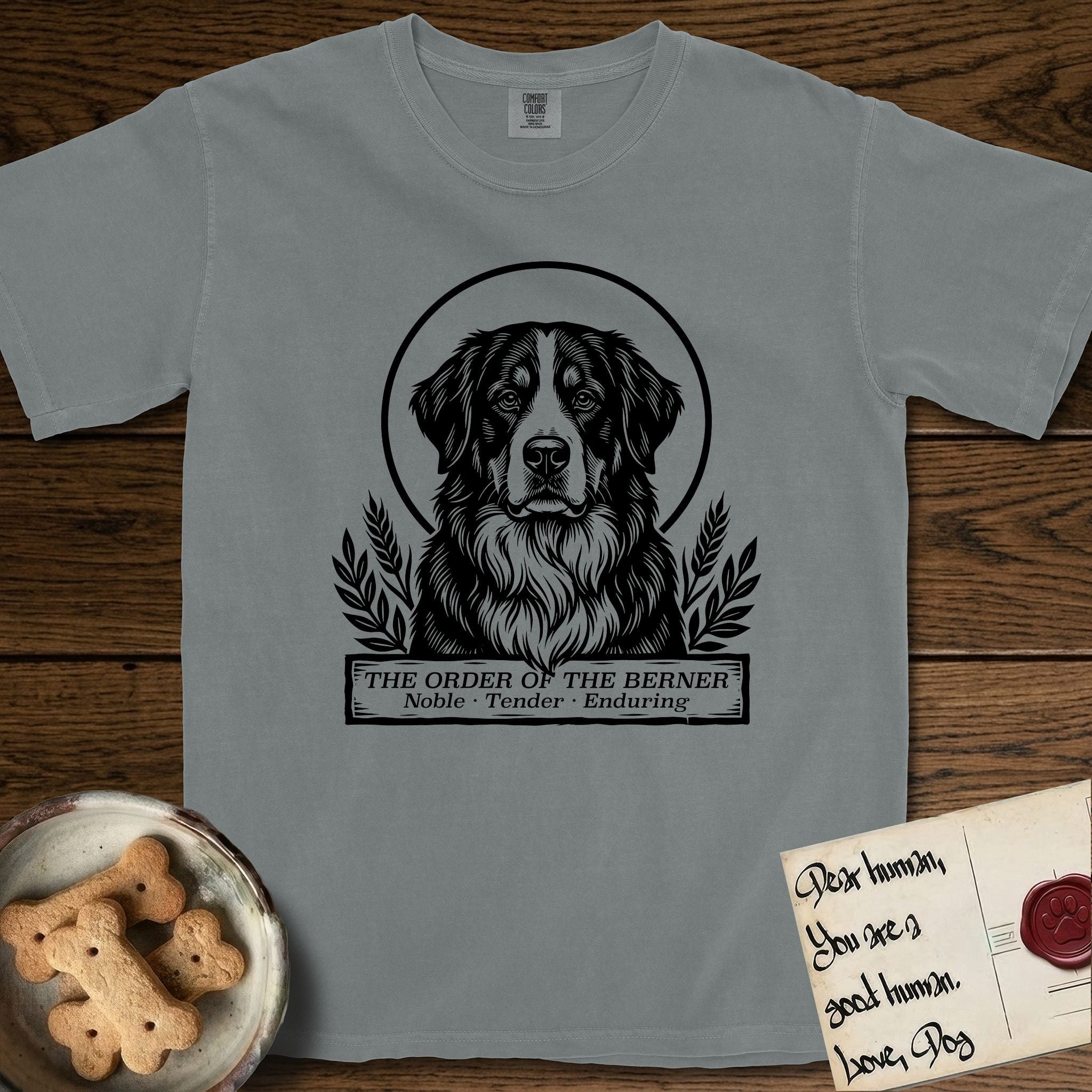 Holy Orders Bernese Mountain Dog T-Shirt flat lay in Granite, featuring a bold black-and-white linocut saint-medallion portrait of a Bernese Mountain Dog.