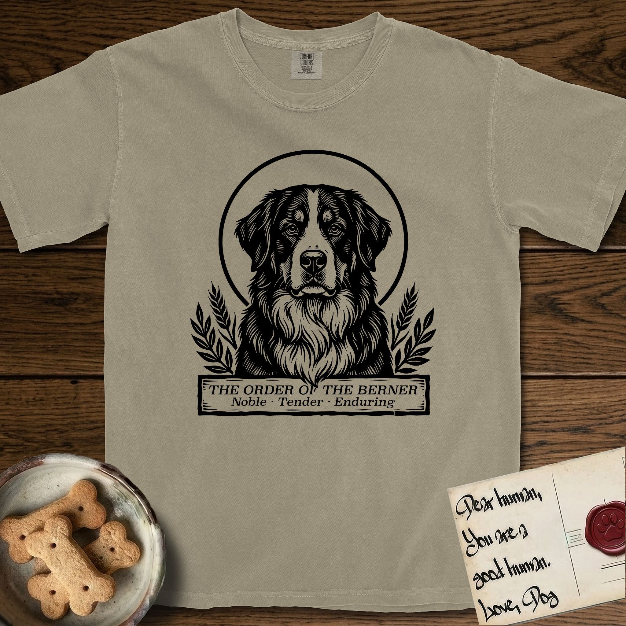 Holy Orders Bernese Mountain Dog T-Shirt flat lay in Khaki, featuring a bold black-and-white linocut saint-medallion portrait of a Bernese Mountain Dog.