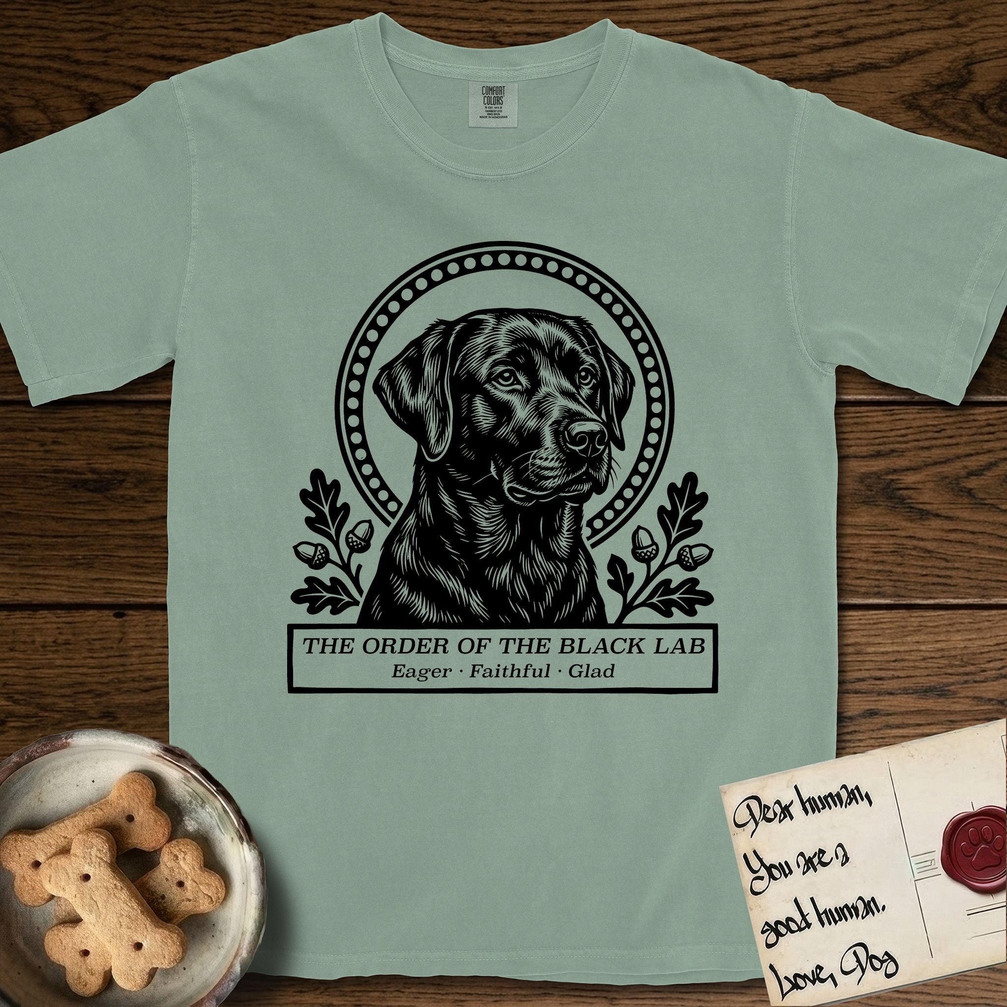 Holy Orders Black Lab T-Shirt flat lay in Bay, featuring a bold black-and-white linocut saint-medallion portrait of a Black Lab.