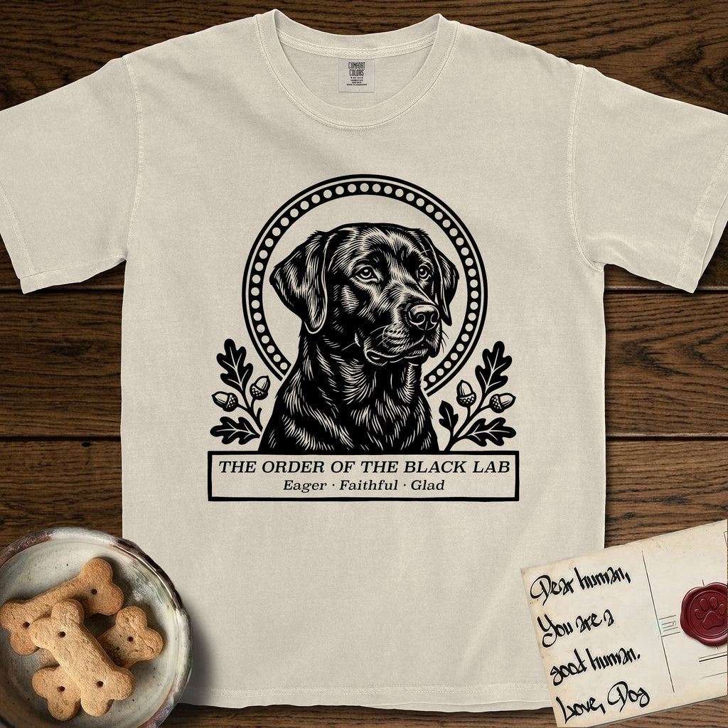 Holy Orders Black Lab T-Shirt flat lay in Ivory, featuring a bold black-and-white linocut saint-medallion portrait of a Black Lab.