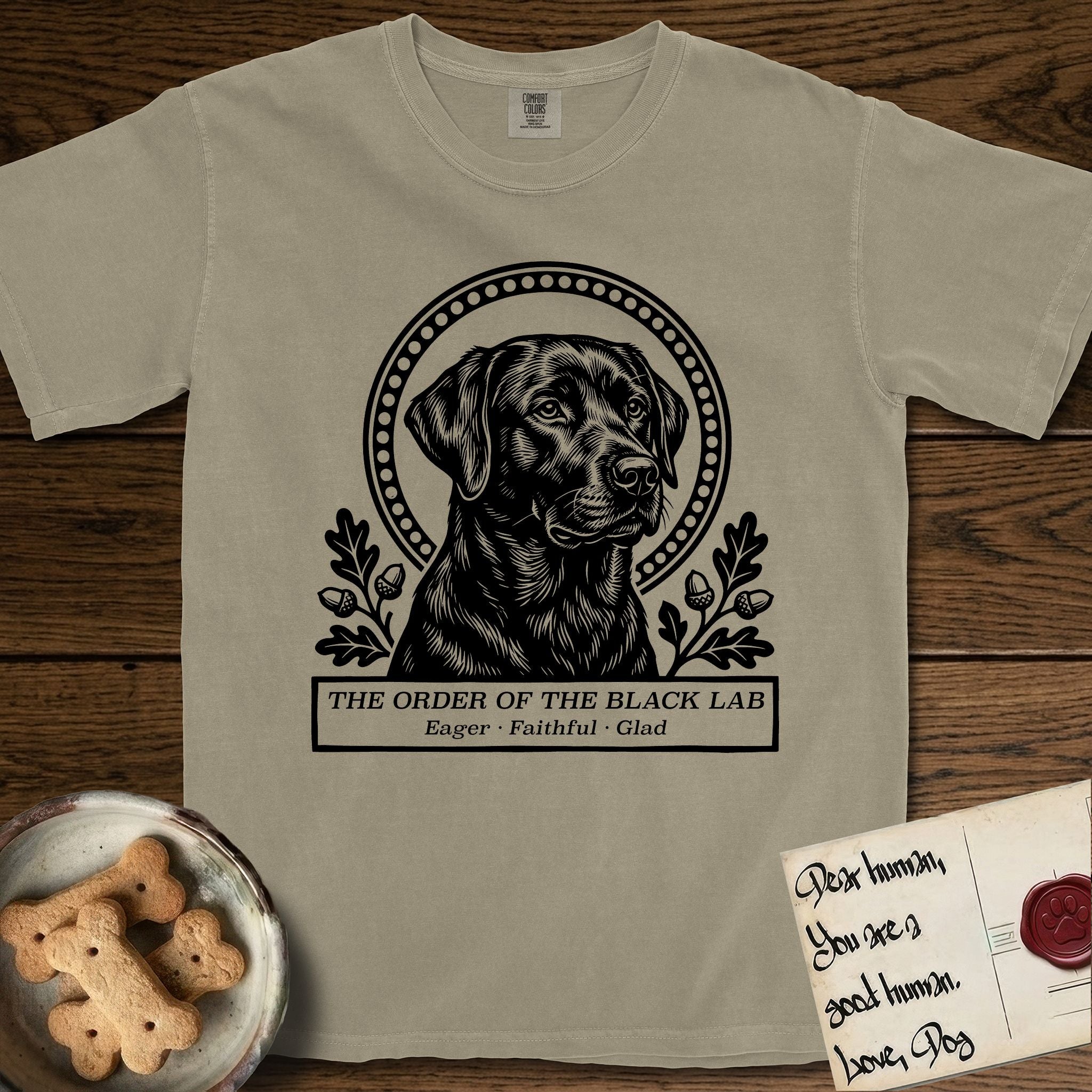 Holy Orders Black Lab T-Shirt flat lay in Khaki, featuring a bold black-and-white linocut saint-medallion portrait of a Black Lab.