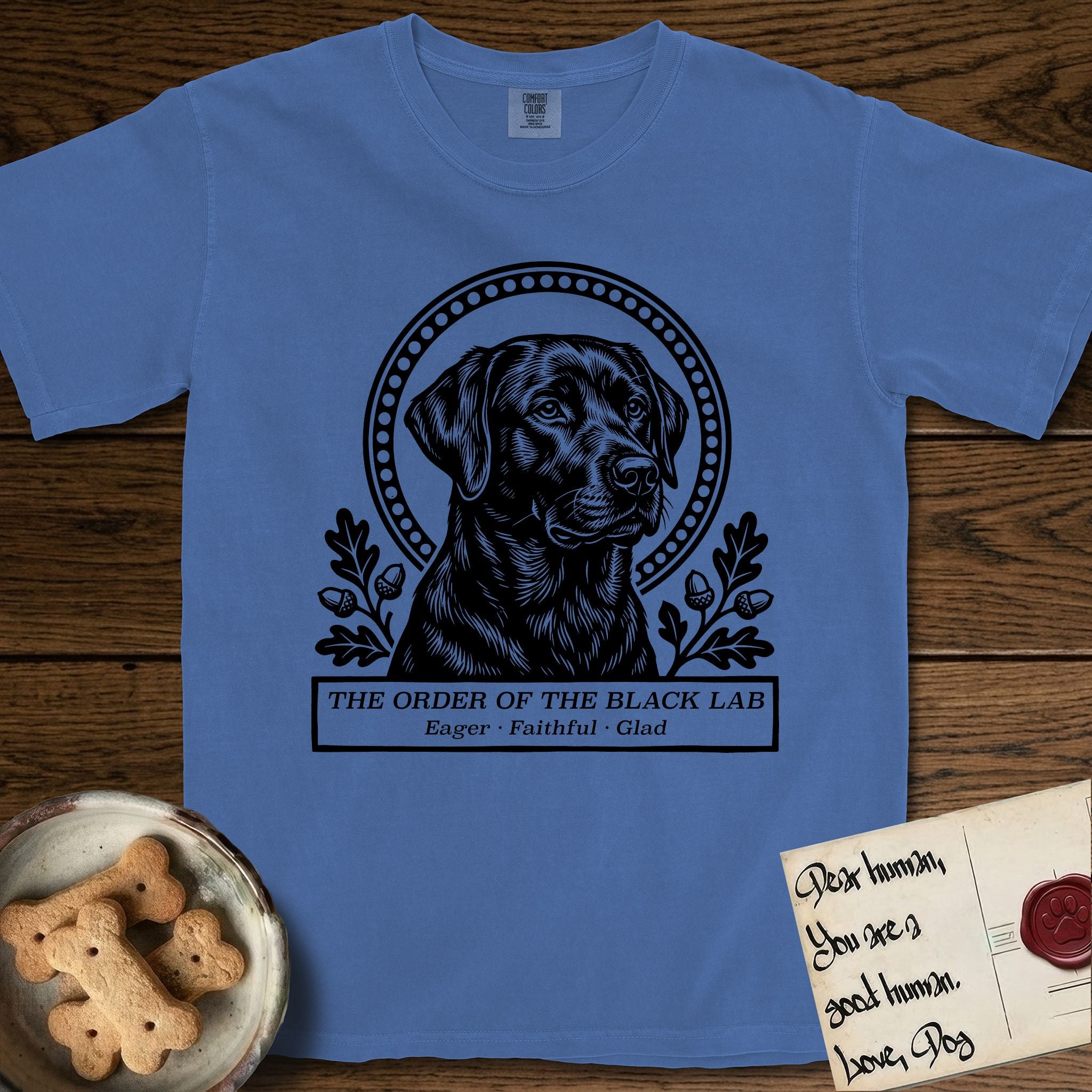 Holy Orders Black Lab T-Shirt flat lay in Mystic Blue, featuring a bold black-and-white linocut saint-medallion portrait of a Black Lab.