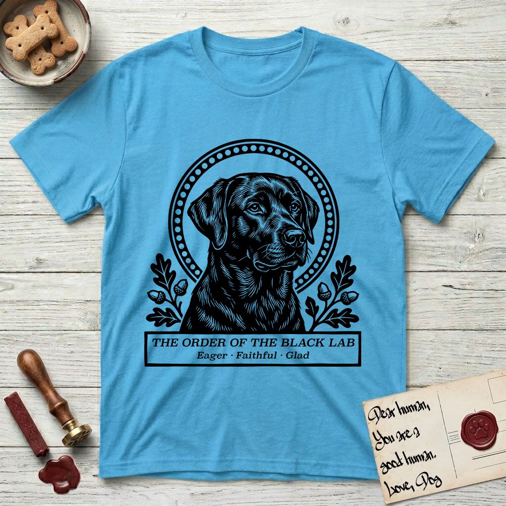 Holy Orders Black Lab T-Shirt flat lay in Sky, featuring a bold black-and-white linocut saint-medallion portrait of a Black Lab.