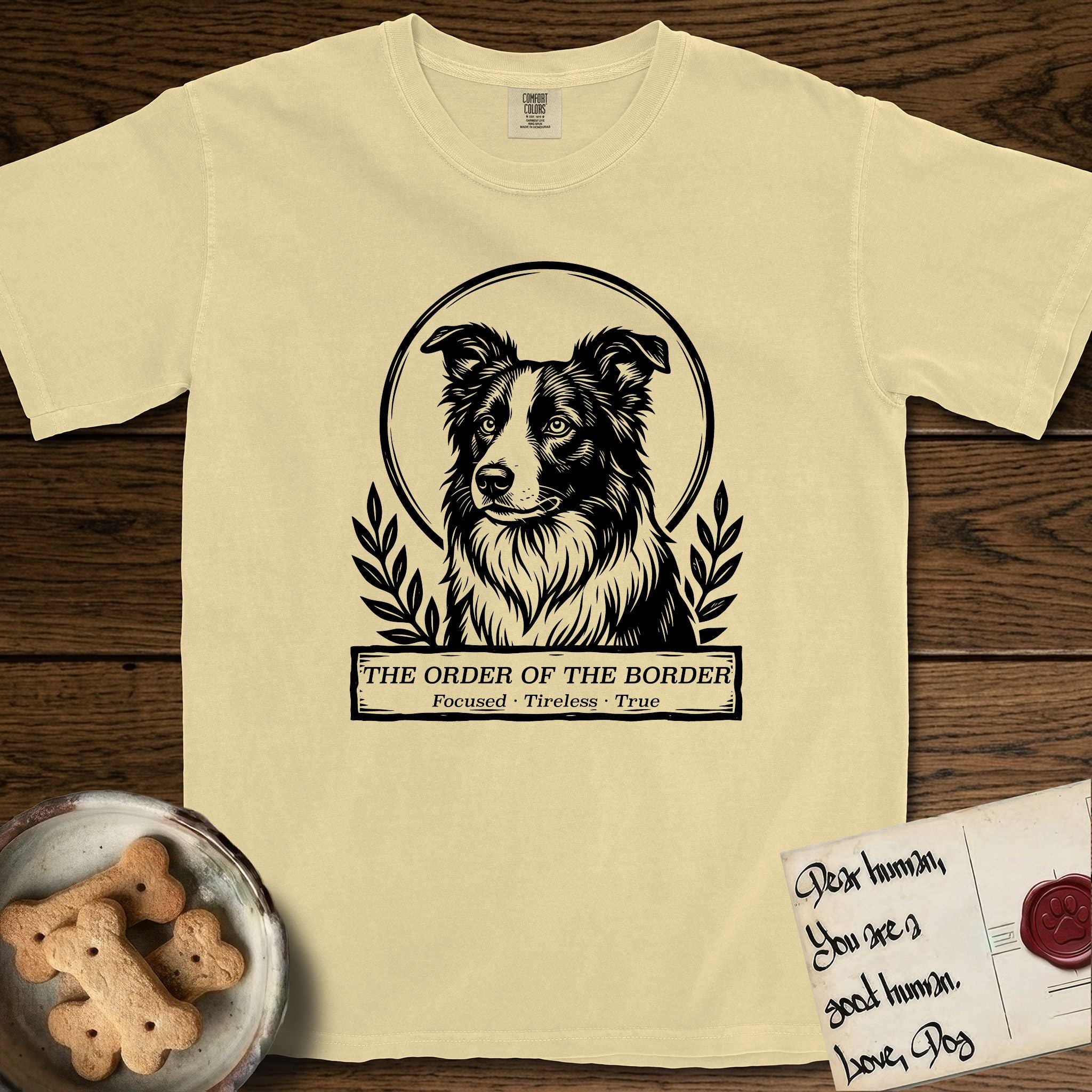 Holy Orders Border Collie T-Shirt flat lay in Butter, featuring a bold black-and-white linocut saint-medallion portrait of a Border Collie.