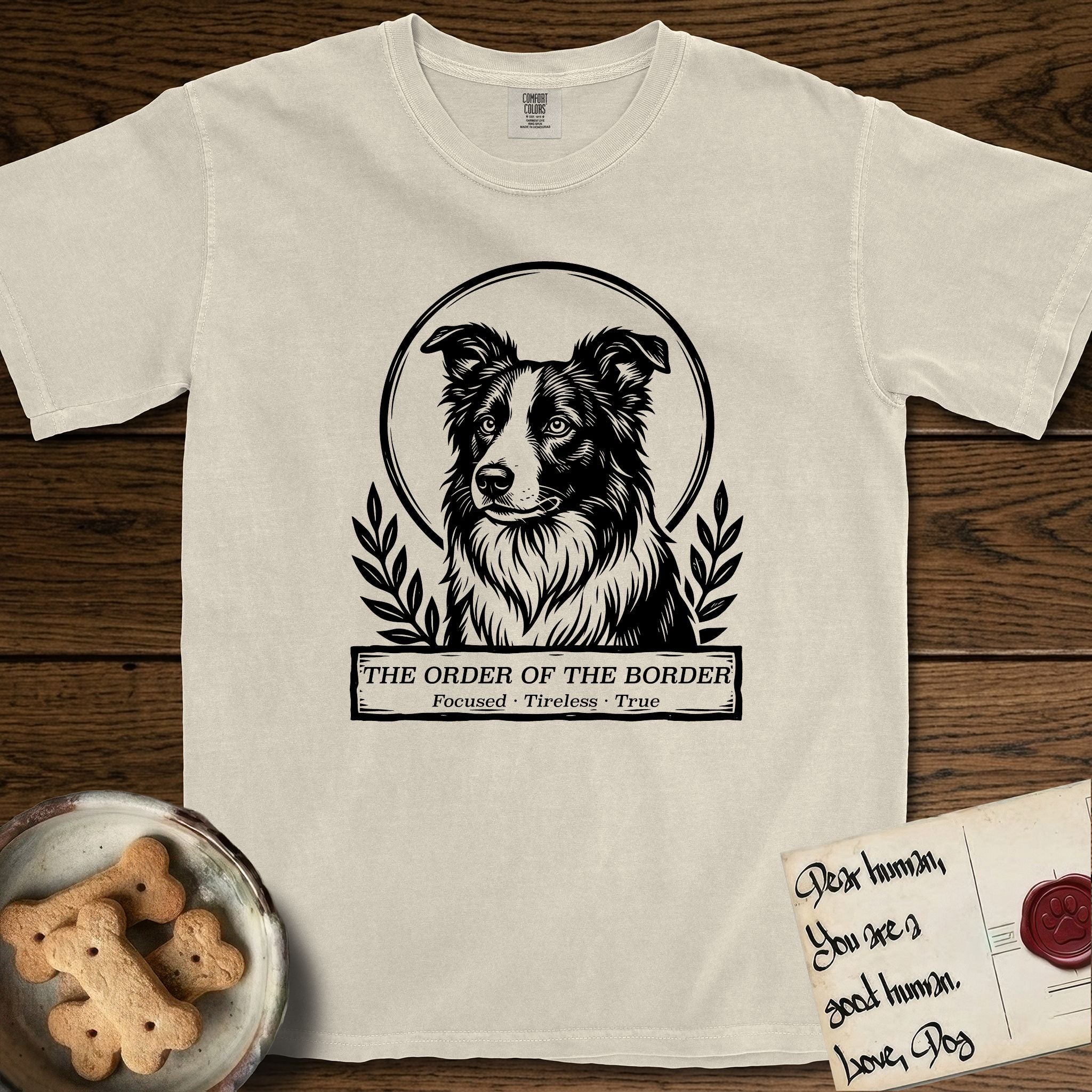 Holy Orders Border Collie T-Shirt flat lay in Ivory, featuring a bold black-and-white linocut saint-medallion portrait of a Border Collie.