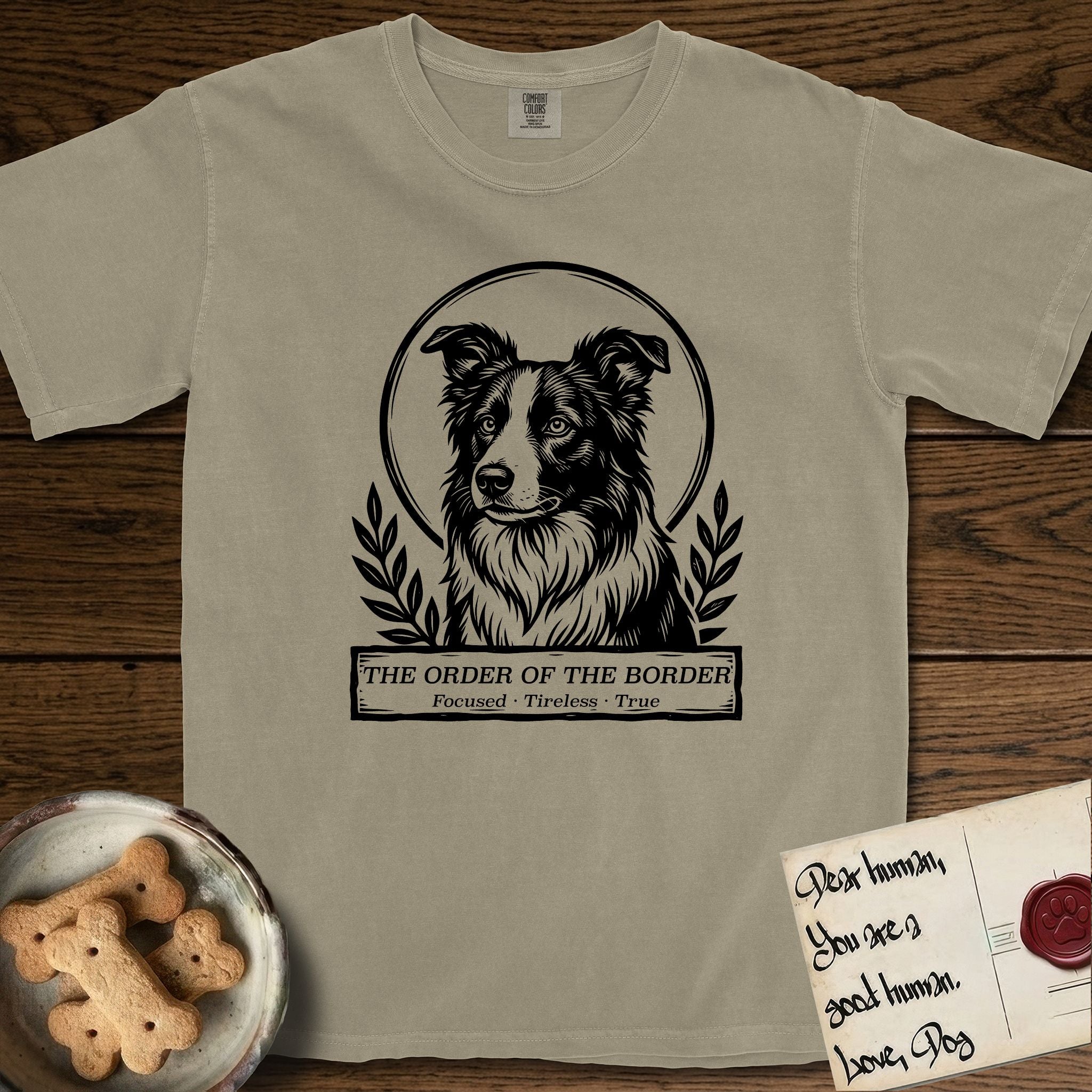 Holy Orders Border Collie T-Shirt flat lay in Khaki, featuring a bold black-and-white linocut saint-medallion portrait of a Border Collie.