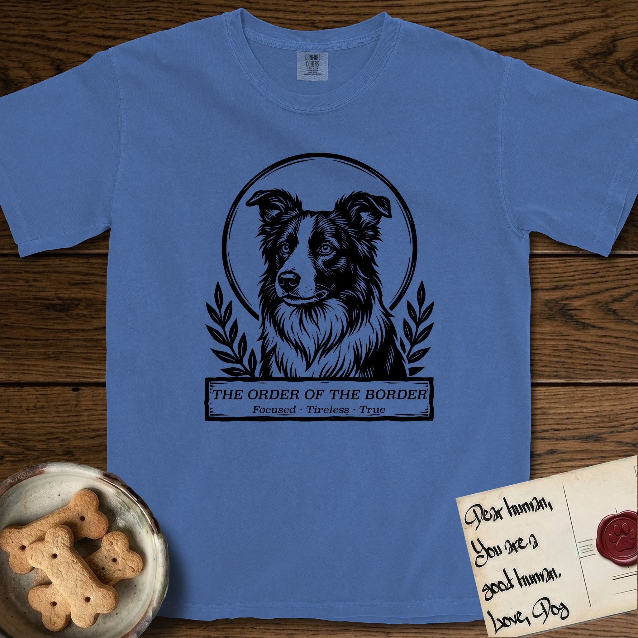 Holy Orders Border Collie T-Shirt flat lay in Mystic Blue, featuring a bold black-and-white linocut saint-medallion portrait of a Border Collie.
