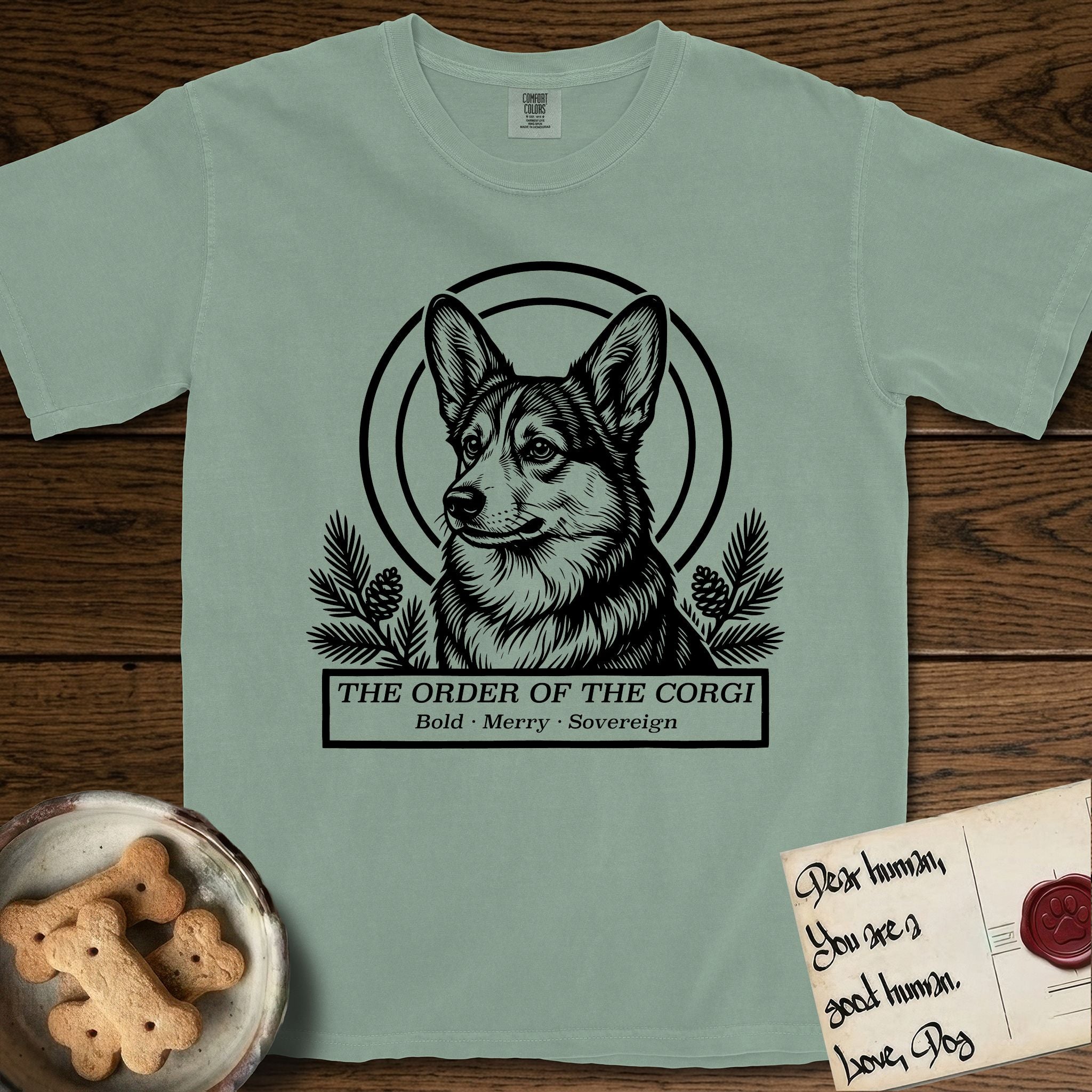 Holy Orders Corgi T-Shirt flat lay in Bay, featuring a bold black-and-white linocut saint-medallion portrait of a Corgi.
