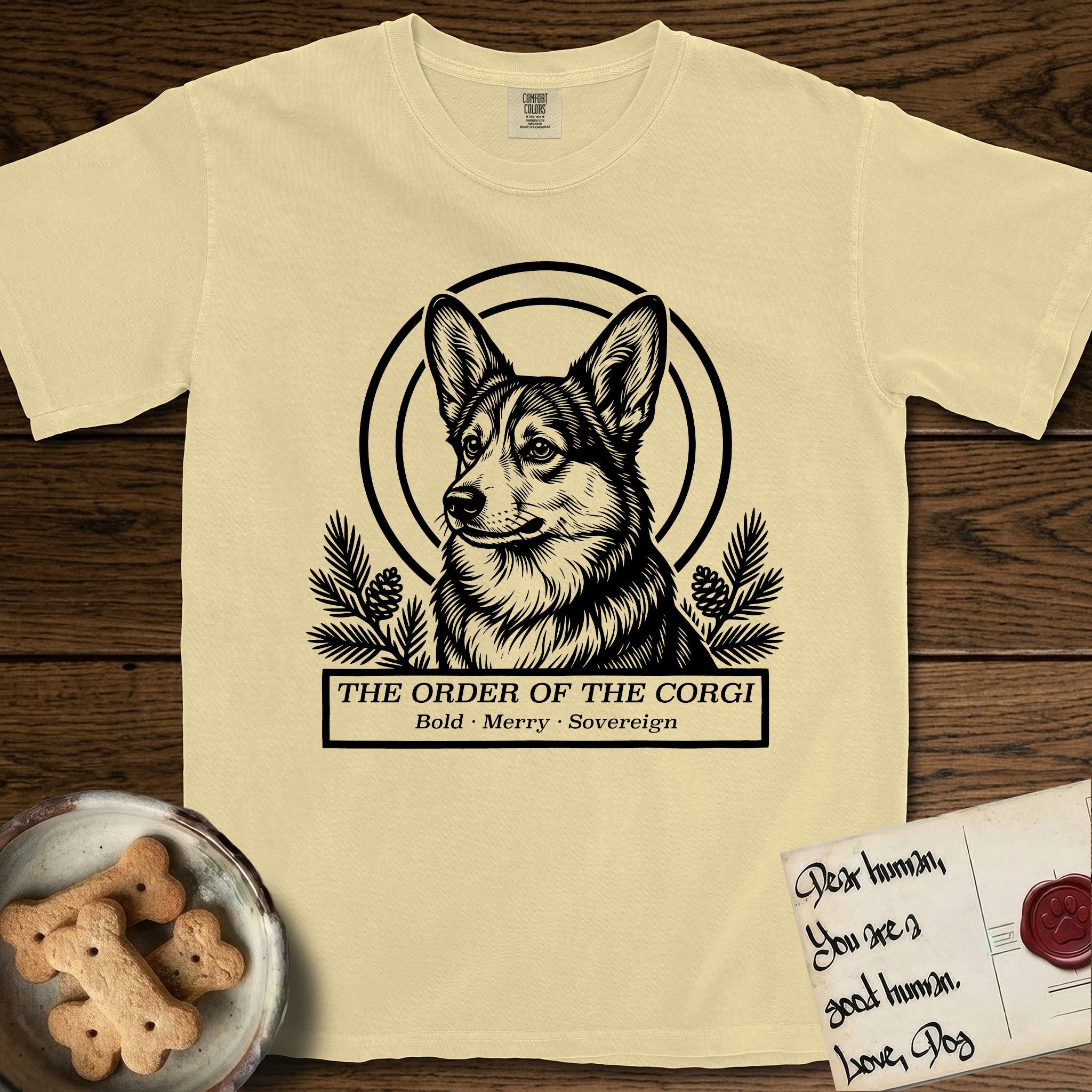 Holy Orders Corgi T-Shirt flat lay in Butter, featuring a bold black-and-white linocut saint-medallion portrait of a Corgi.