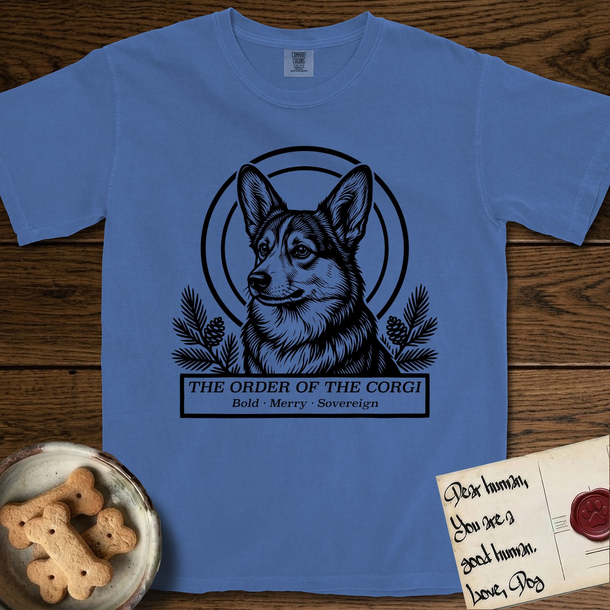 Holy Orders Corgi T-Shirt flat lay in Mystic Blue, featuring a bold black-and-white linocut saint-medallion portrait of a Corgi.