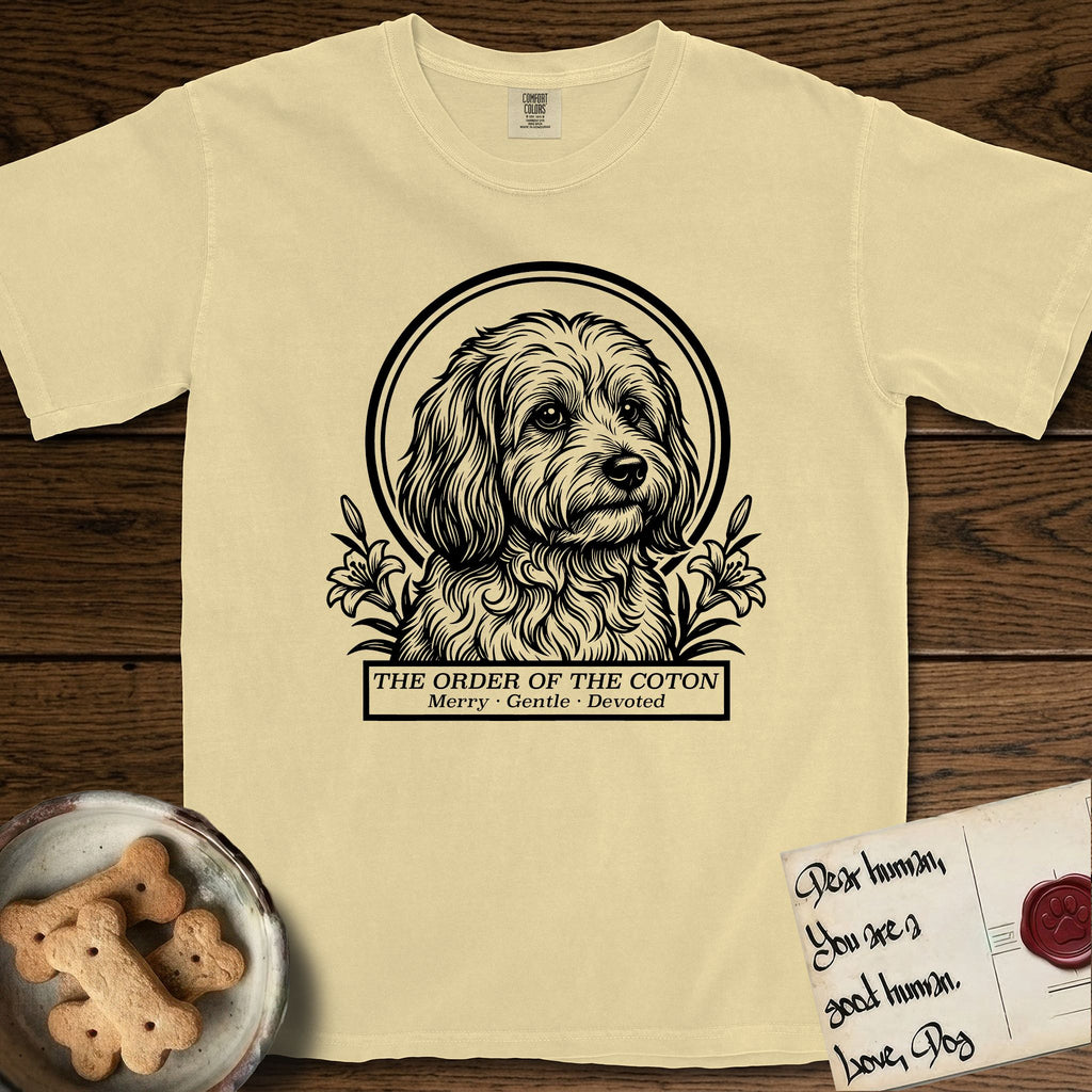 Holy Orders Coton T-Shirt flat lay in Butter, featuring a bold black-and-white linocut saint-medallion portrait of a Coton de Tulear.