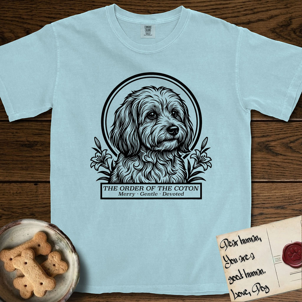 Holy Orders Coton T-Shirt flat lay in Chambray, featuring a bold black-and-white linocut saint-medallion portrait of a Coton de Tulear.