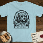 Holy Orders Coton T-Shirt flat lay in Chambray, featuring a bold black-and-white linocut saint-medallion portrait of a Coton de Tulear.