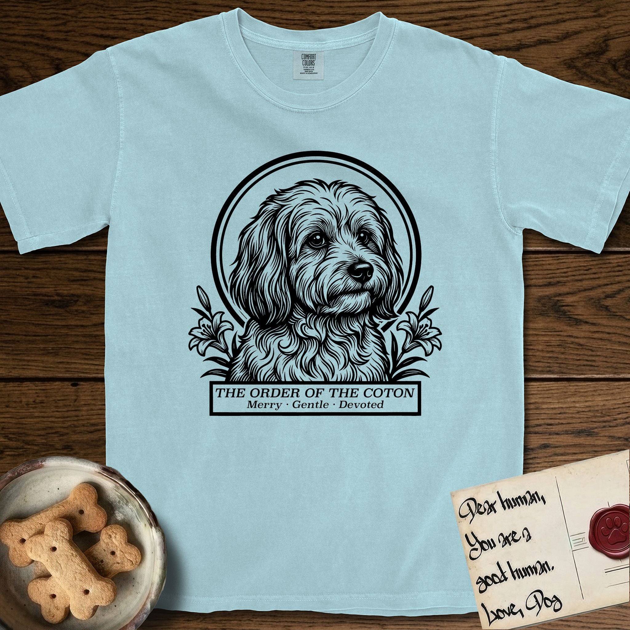 Holy Orders Coton T-Shirt flat lay in Chambray, featuring a bold black-and-white linocut saint-medallion portrait of a Coton de Tulear.
