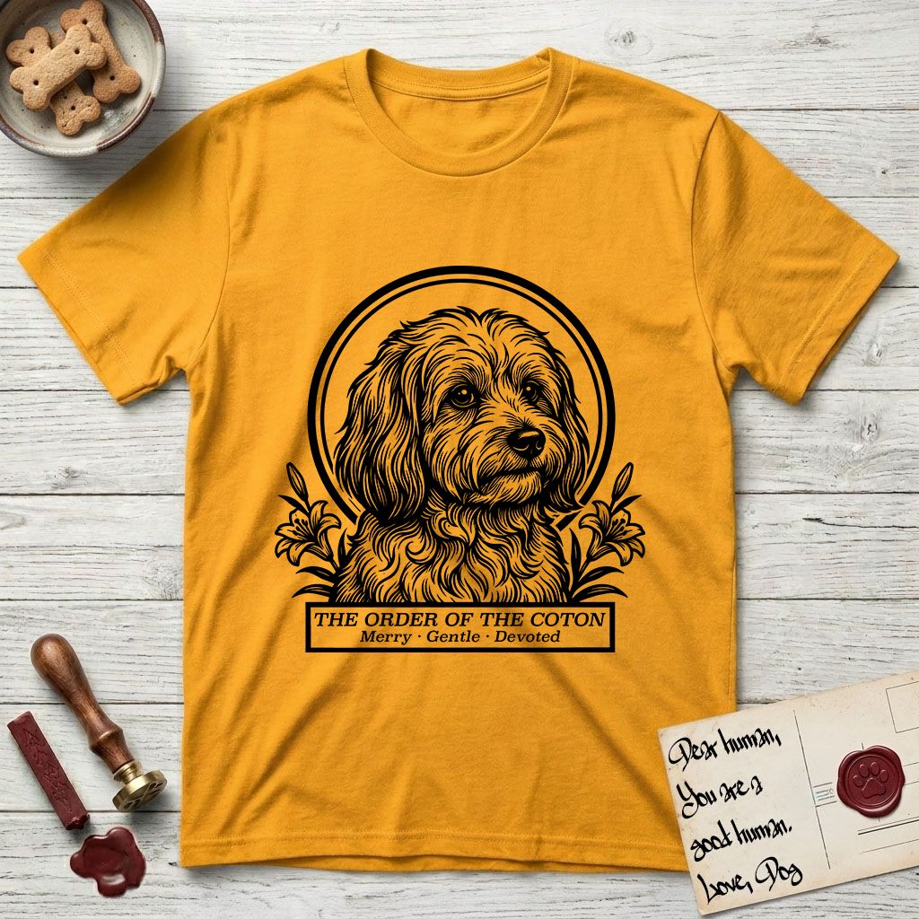 Holy Orders Coton T-Shirt flat lay in Gold, featuring a bold black-and-white linocut saint-medallion portrait of a Coton de Tulear.