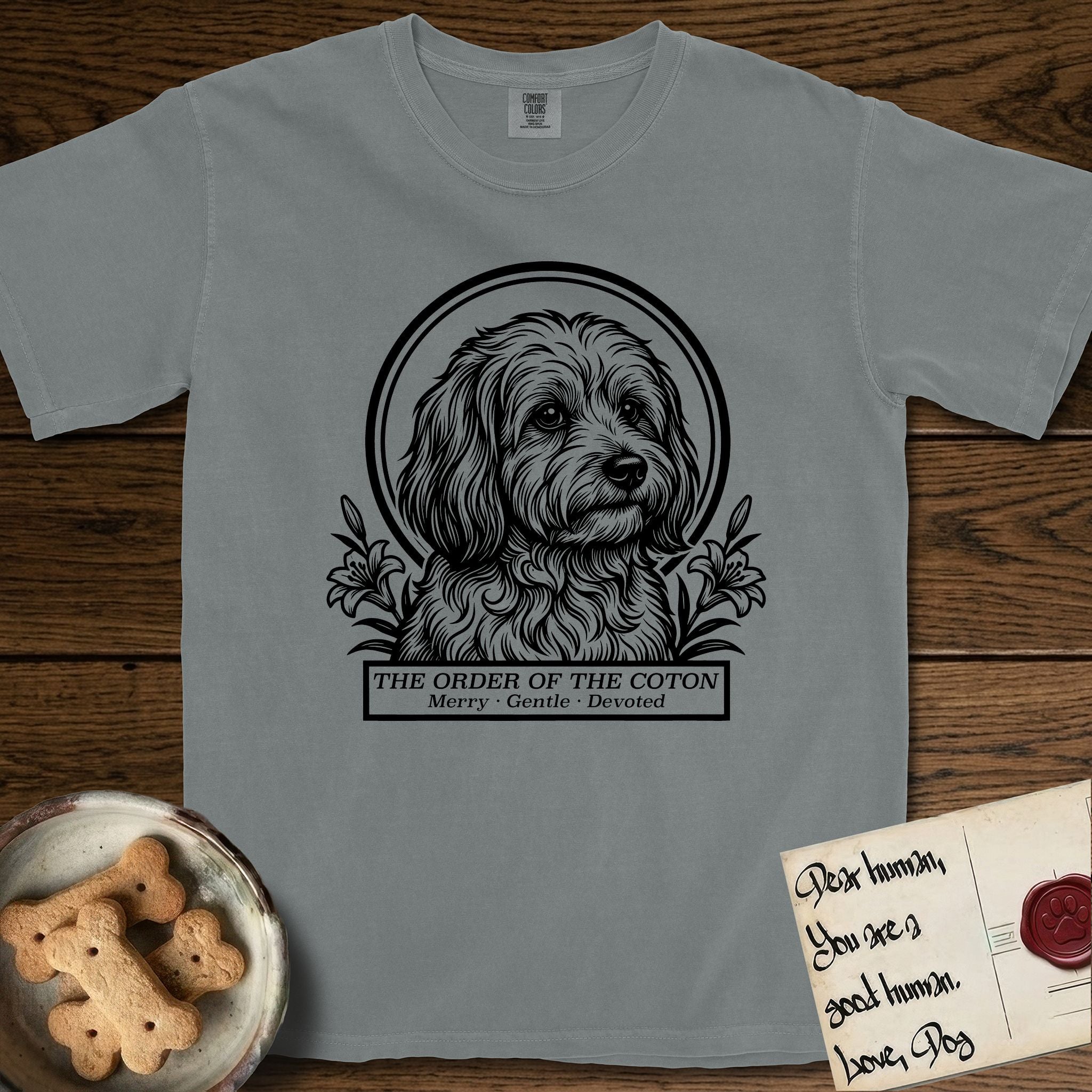 Holy Orders Coton T-Shirt flat lay in Granite, featuring a bold black-and-white linocut saint-medallion portrait of a Coton de Tulear.