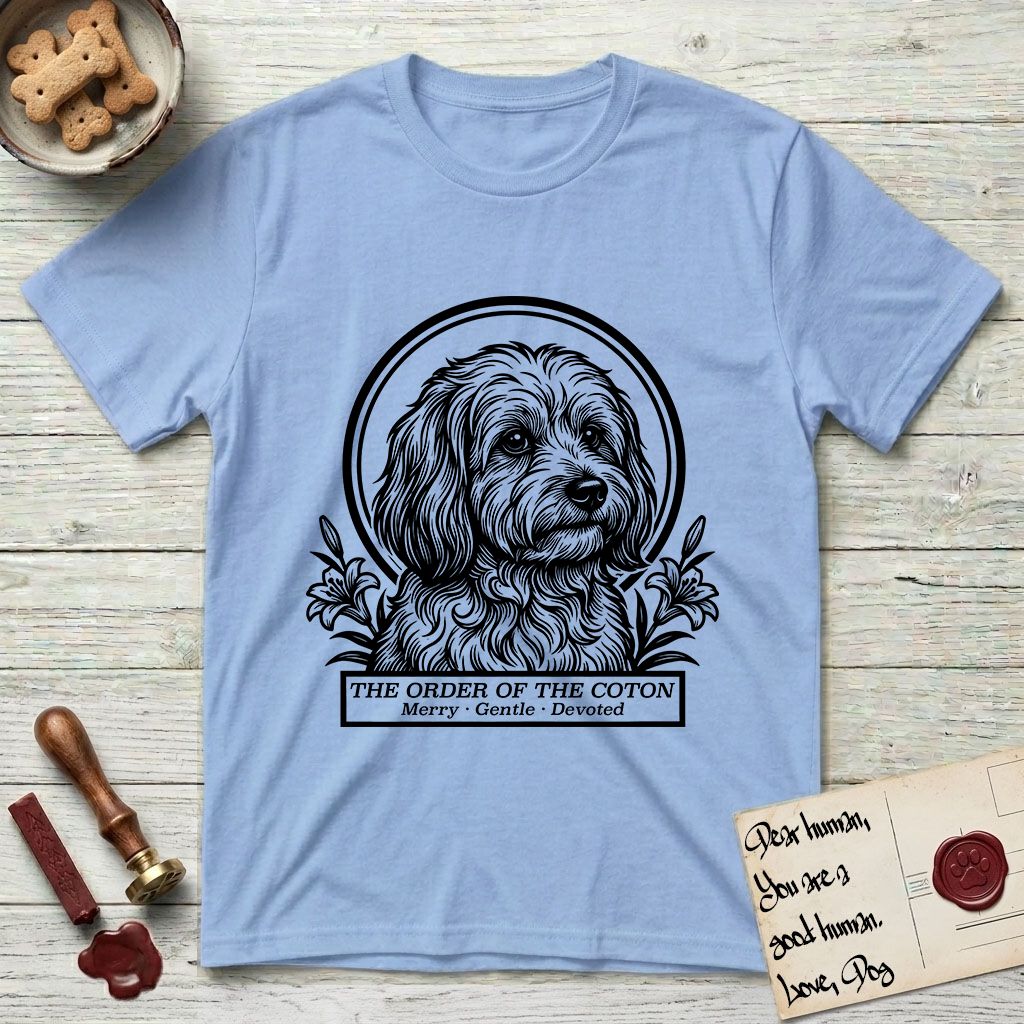 Holy Orders Coton T-Shirt flat lay in Light Blue, featuring a bold black-and-white linocut saint-medallion portrait of a Coton de Tulear.