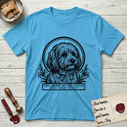 Holy Orders Coton T-Shirt flat lay in Sky, featuring a bold black-and-white linocut saint-medallion portrait of a Coton de Tulear.