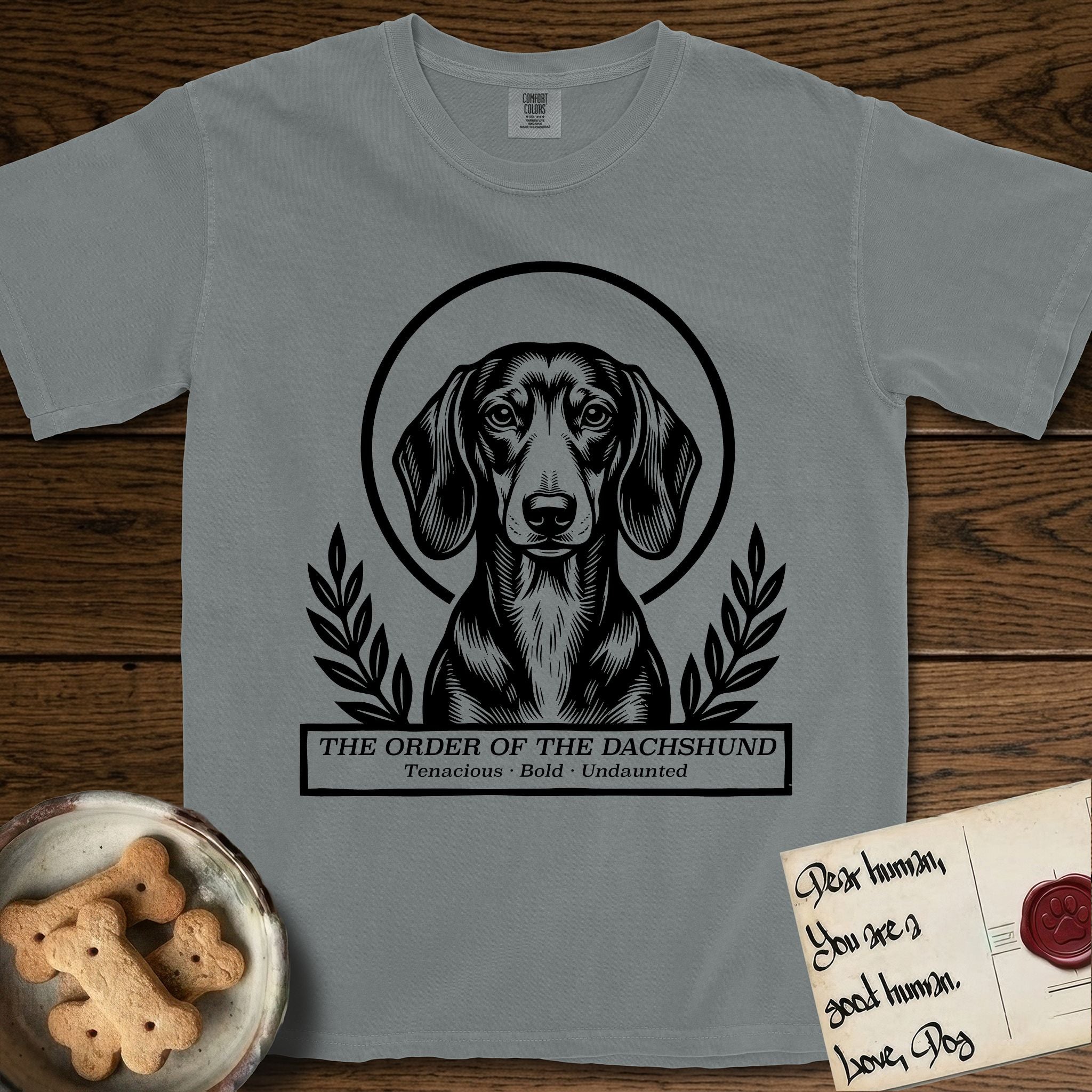 Holy Orders Dachshund T-Shirt flat lay in Granite, featuring a bold black-and-white linocut saint-medallion portrait of a Dachshund.
