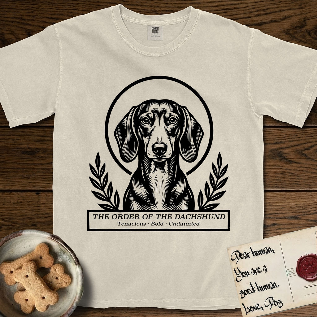 Holy Orders Dachshund T-Shirt flat lay in Ivory, featuring a bold black-and-white linocut saint-medallion portrait of a Dachshund.