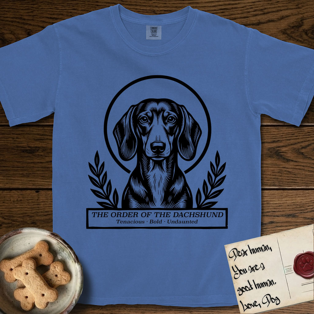 Holy Orders Dachshund T-Shirt flat lay in Mystic Blue, featuring a bold black-and-white linocut saint-medallion portrait of a Dachshund.