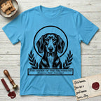 Holy Orders Dachshund T-Shirt flat lay in Sky, featuring a bold black-and-white linocut saint-medallion portrait of a Dachshund.