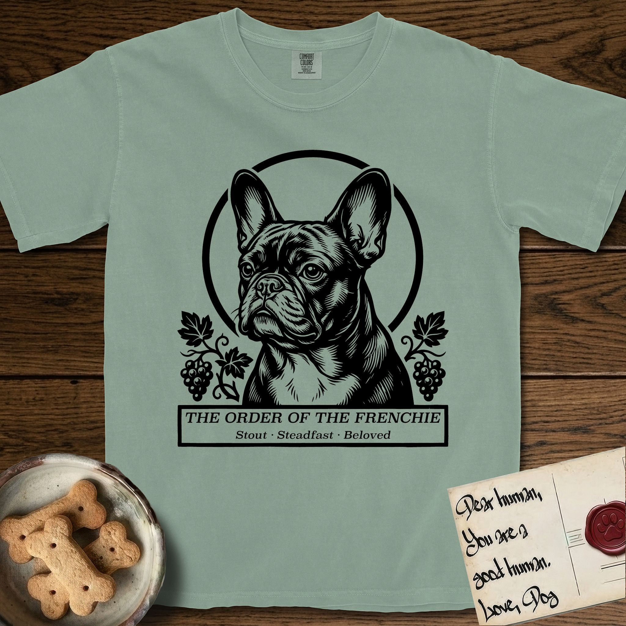 Holy Orders French Bulldog T-Shirt flat lay in Bay, featuring a bold black-and-white linocut saint-medallion portrait of a French Bulldog.