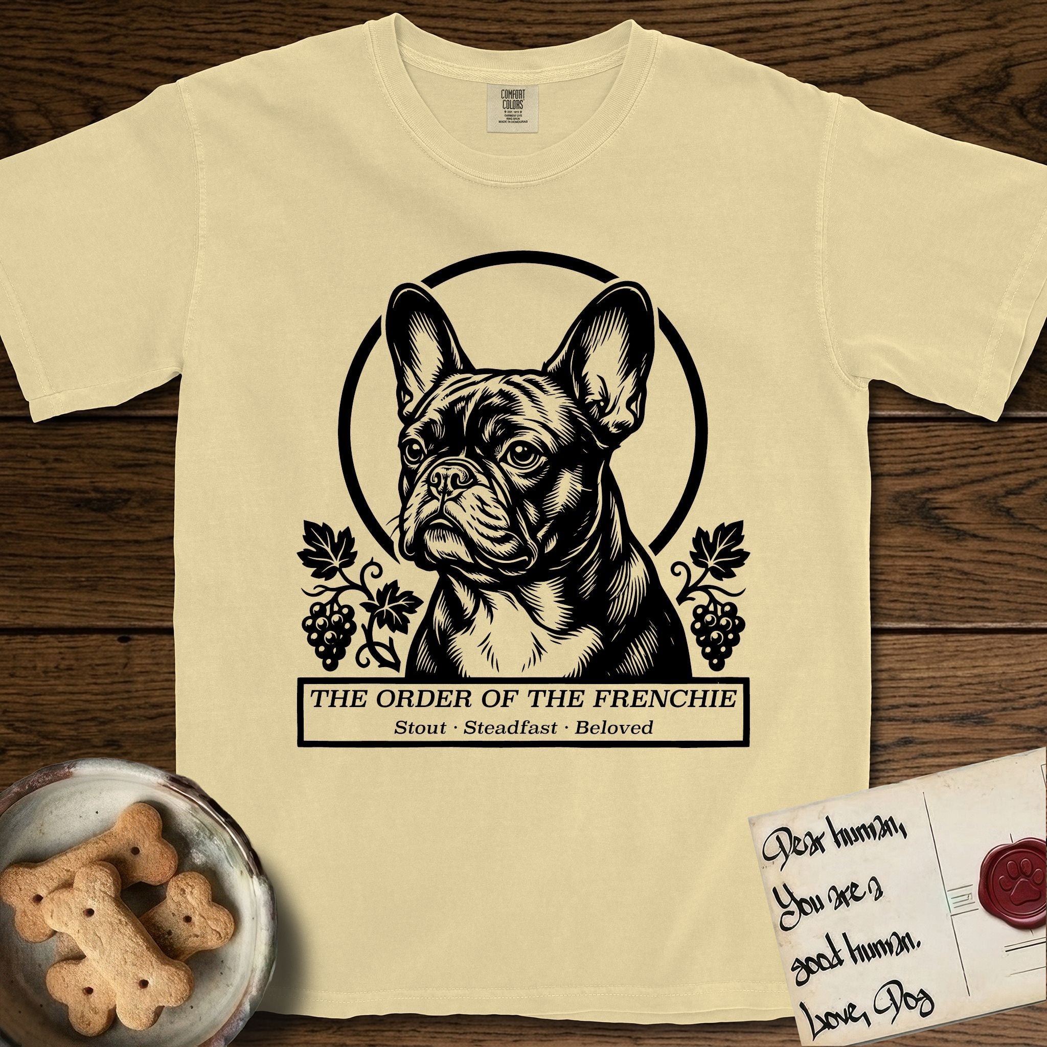 Holy Orders French Bulldog T-Shirt flat lay in Butter, featuring a bold black-and-white linocut saint-medallion portrait of a French Bulldog.
