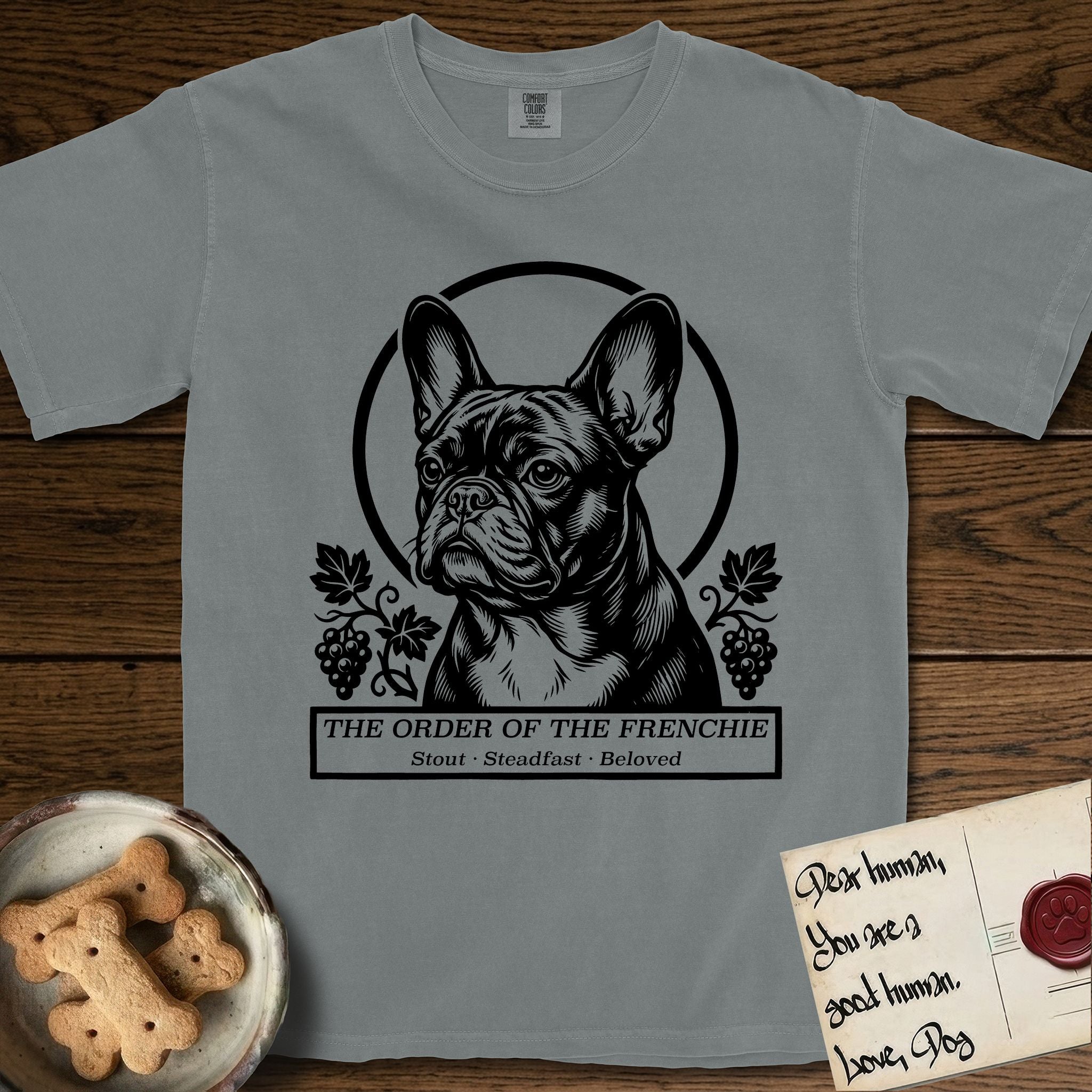 Holy Orders French Bulldog T-Shirt flat lay in Granite, featuring a bold black-and-white linocut saint-medallion portrait of a French Bulldog.