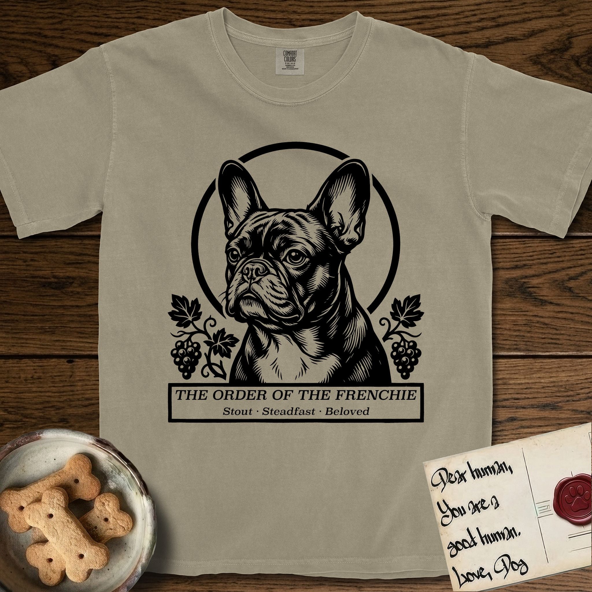 Holy Orders French Bulldog T-Shirt flat lay in Khaki, featuring a bold black-and-white linocut saint-medallion portrait of a French Bulldog.