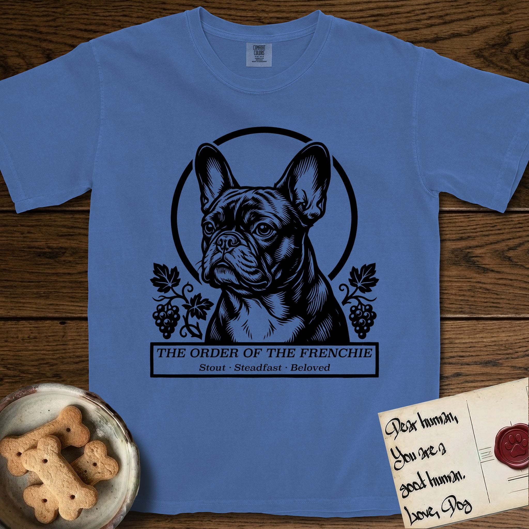Holy Orders French Bulldog T-Shirt flat lay in Mystic Blue, featuring a bold black-and-white linocut saint-medallion portrait of a French Bulldog.