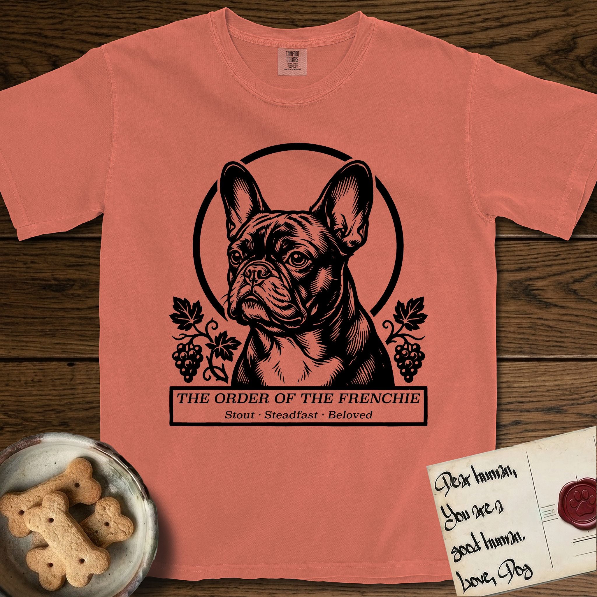 Holy Orders French Bulldog T-Shirt flat lay in Terracotta, featuring a bold black-and-white linocut saint-medallion portrait of a French Bulldog.