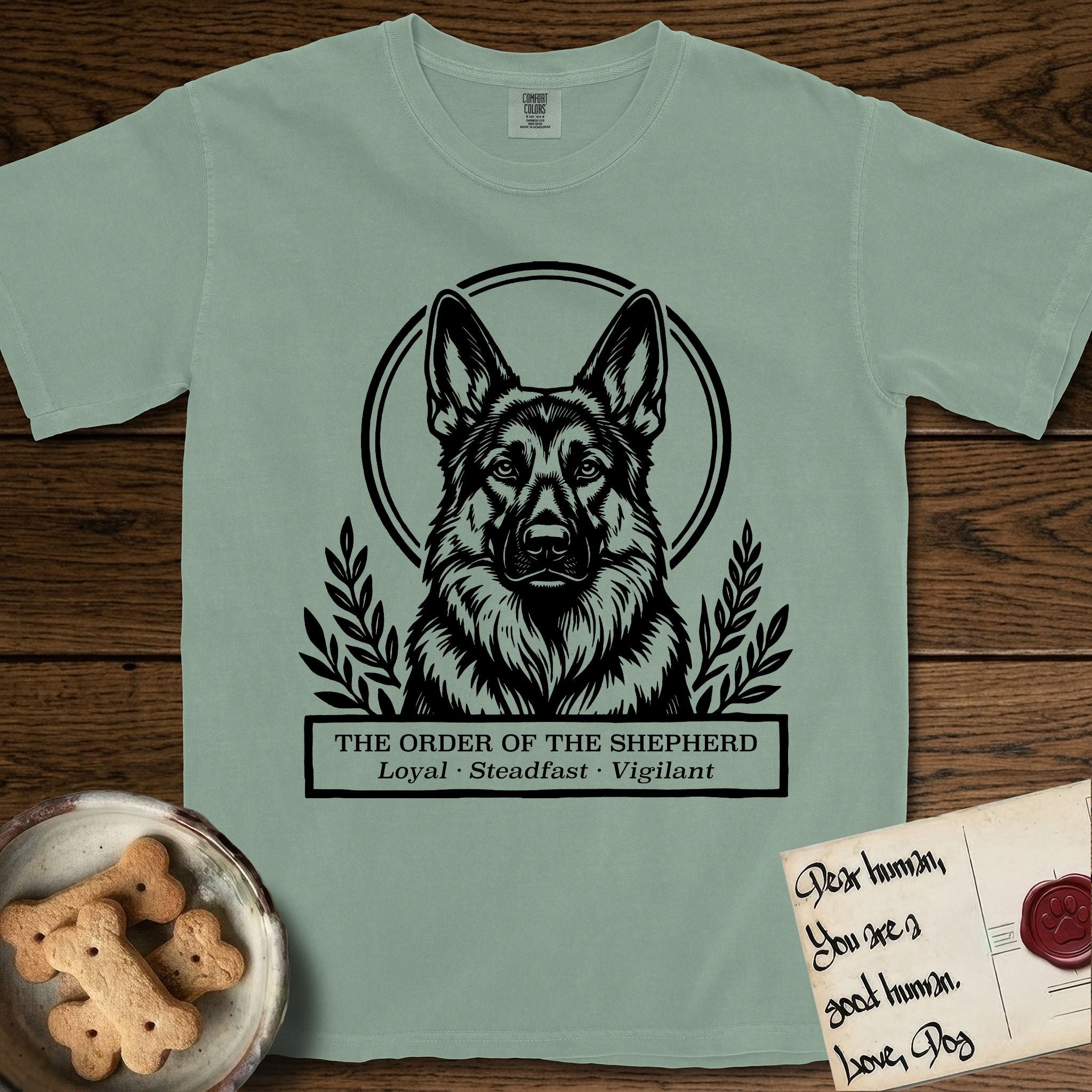 Holy Orders German Shepherd T-Shirt flat lay in Bay, featuring a bold black-and-white linocut saint-medallion portrait of a German Shepherd.