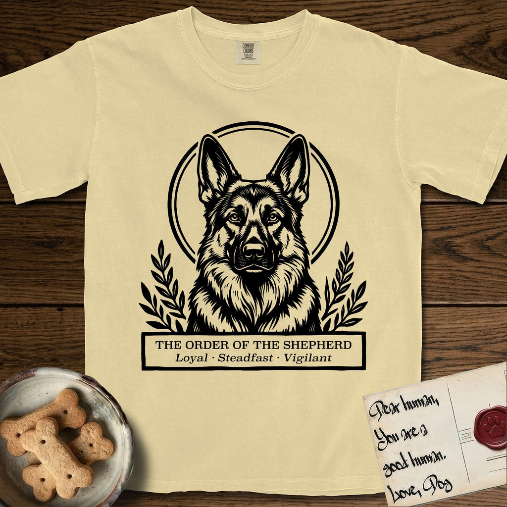 Holy Orders German Shepherd T-Shirt flat lay in Butter, featuring a bold black-and-white linocut saint-medallion portrait of a German Shepherd.