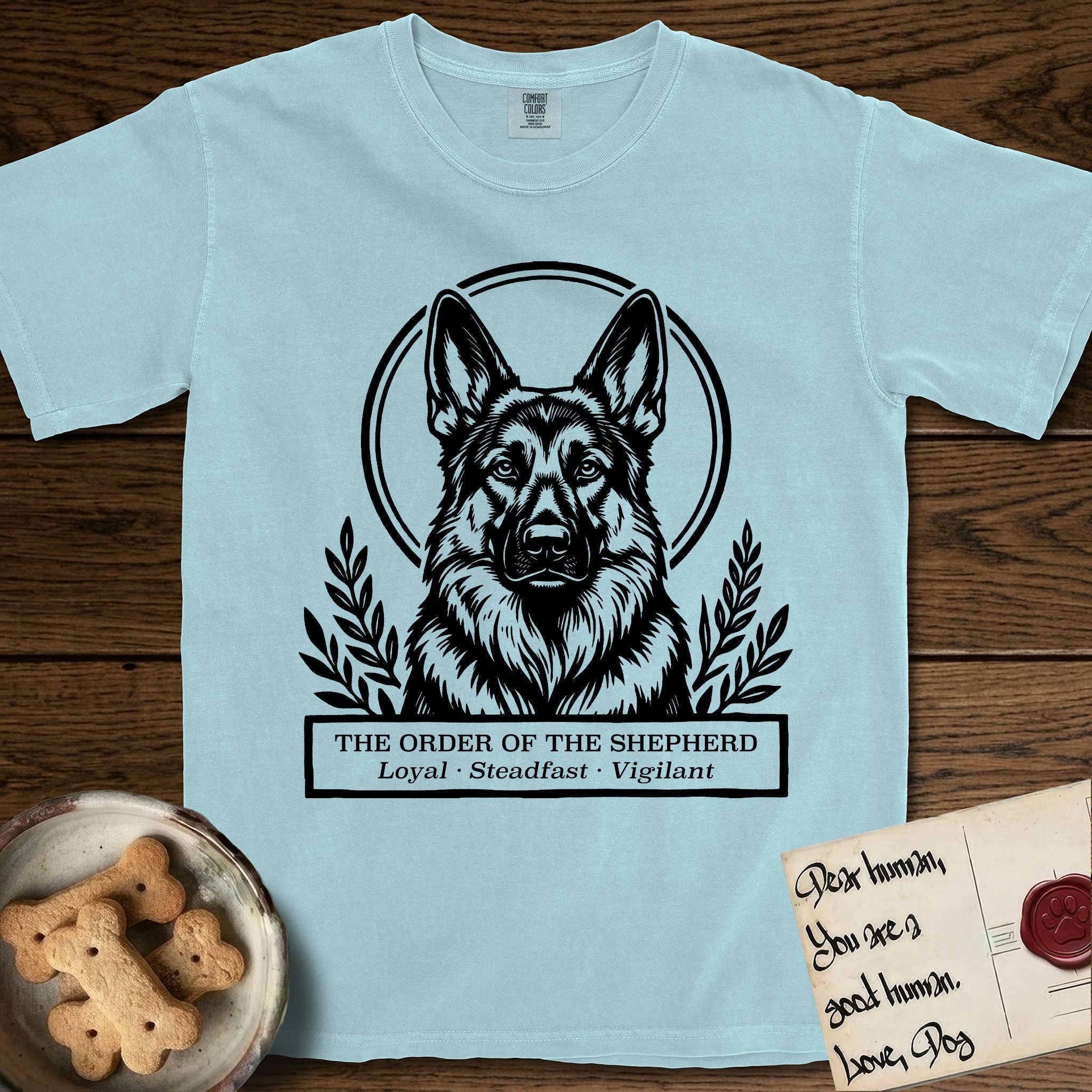 Holy Orders German Shepherd T-Shirt flat lay in Chambray, featuring a bold black-and-white linocut saint-medallion portrait of a German Shepherd.