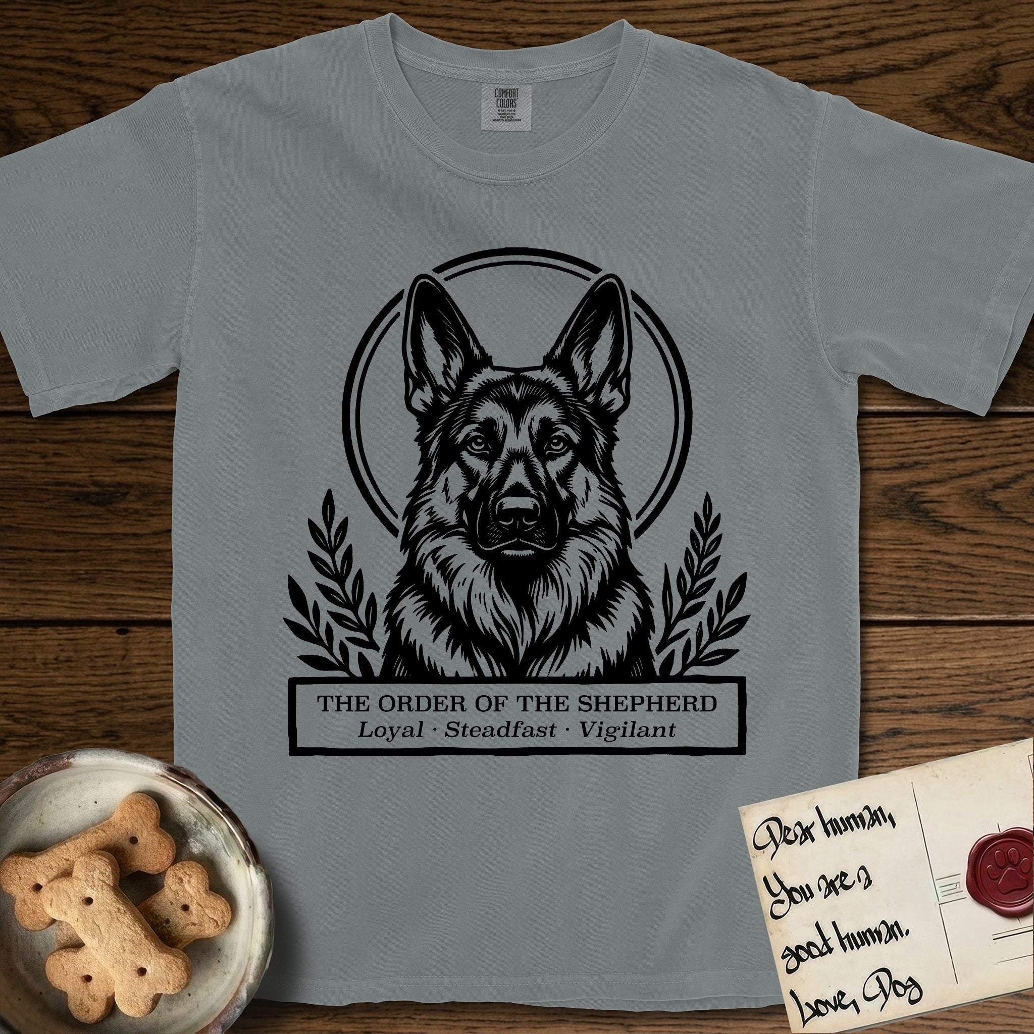 Holy Orders German Shepherd T-Shirt flat lay in Granite, featuring a bold black-and-white linocut saint-medallion portrait of a German Shepherd.