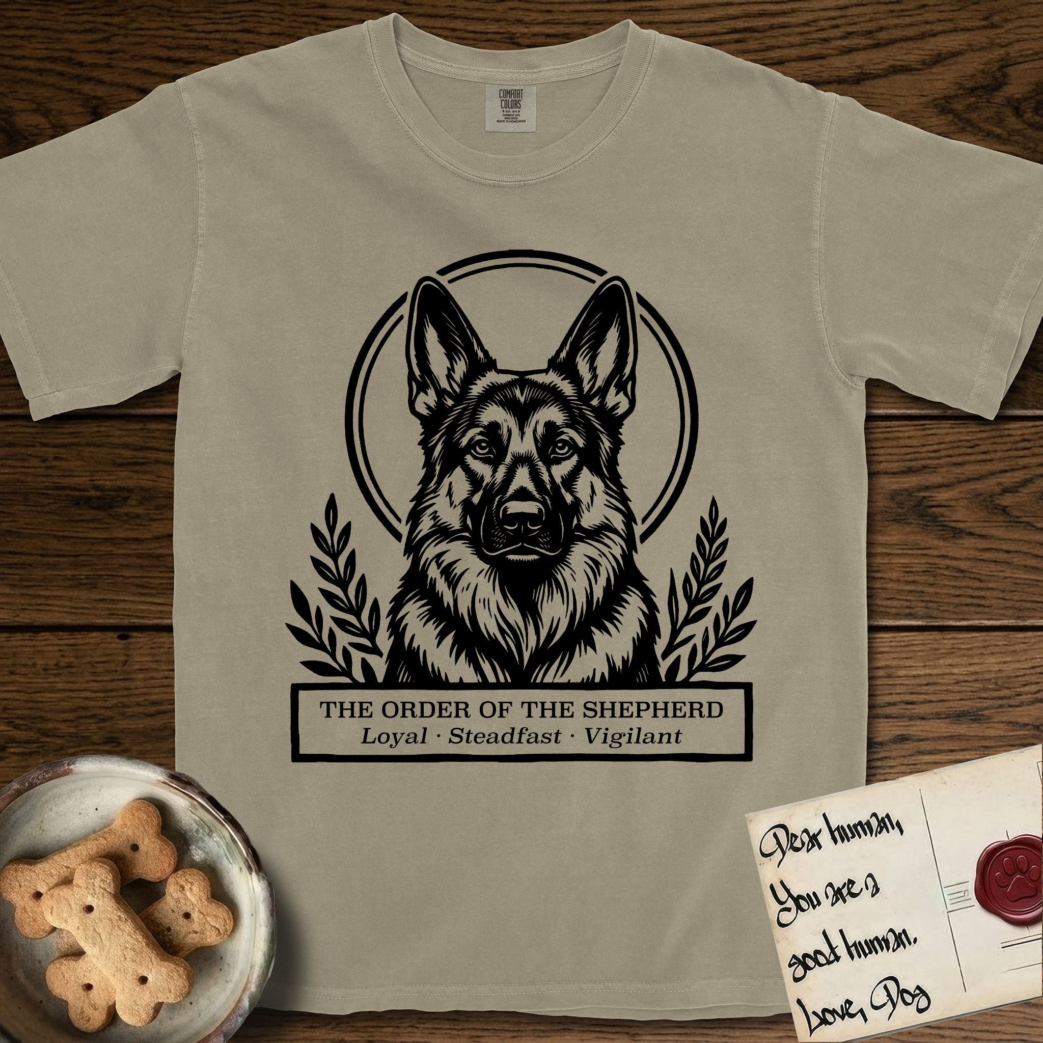 Holy Orders German Shepherd T-Shirt flat lay in Khaki, featuring a bold black-and-white linocut saint-medallion portrait of a German Shepherd.
