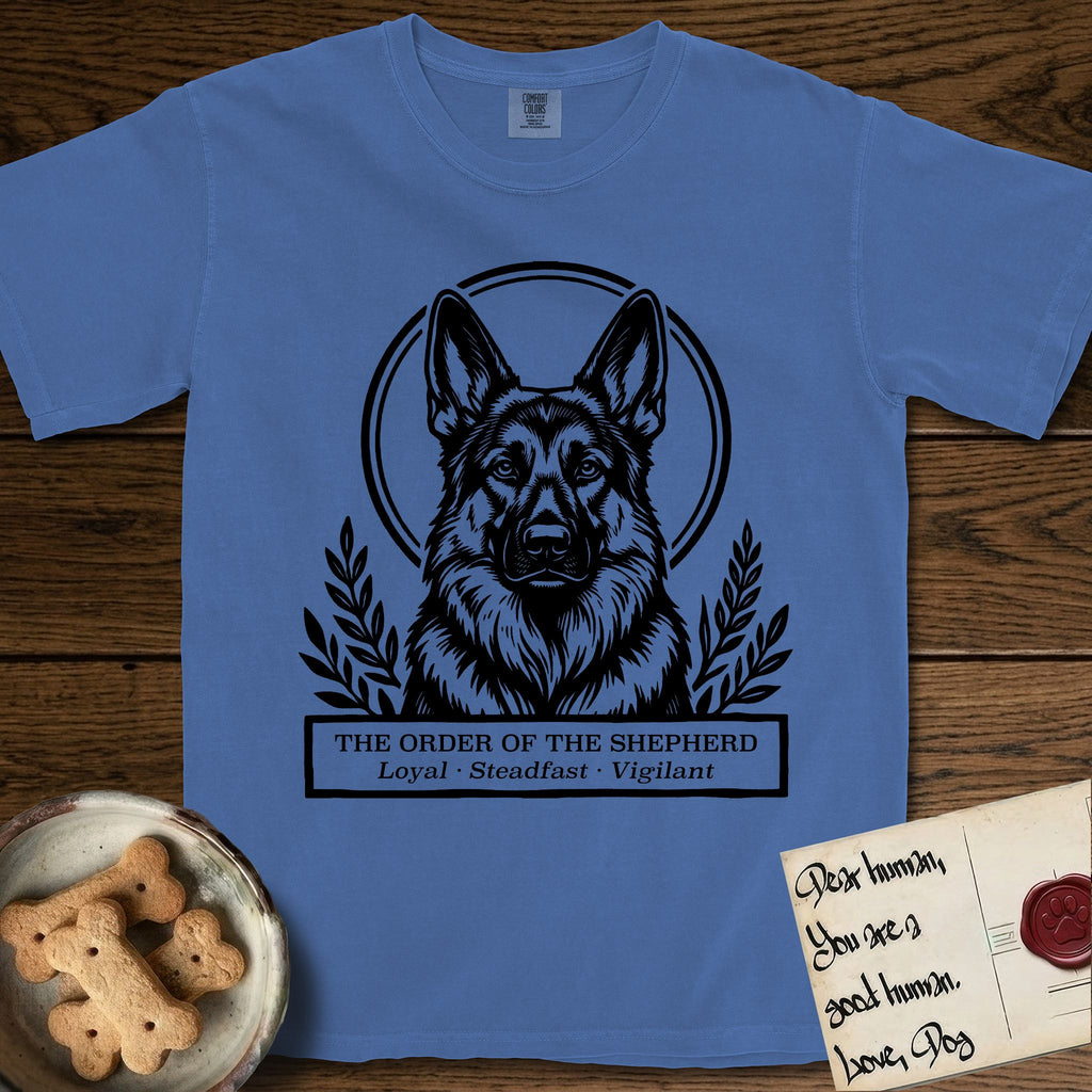 Holy Orders German Shepherd T-Shirt flat lay in Mystic Blue, featuring a bold black-and-white linocut saint-medallion portrait of a German Shepherd.