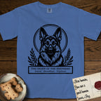 Holy Orders German Shepherd T-Shirt flat lay in Mystic Blue, featuring a bold black-and-white linocut saint-medallion portrait of a German Shepherd.