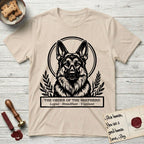 Holy Orders German Shepherd T-Shirt flat lay in Sand, featuring a bold black-and-white linocut saint-medallion portrait of a German Shepherd.
