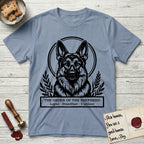 Holy Orders German Shepherd T-Shirt flat lay in Stone Blue, featuring a bold black-and-white linocut saint-medallion portrait of a German Shepherd.
