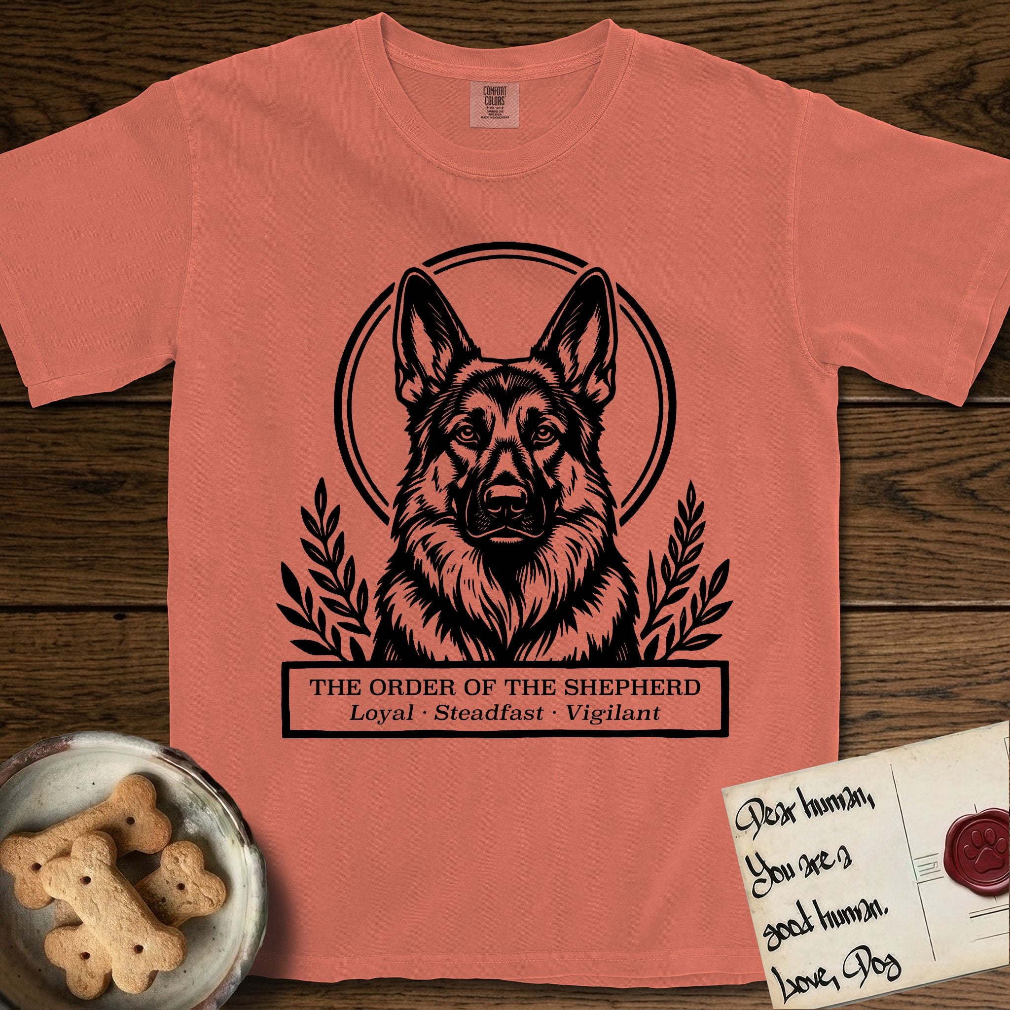 Holy Orders German Shepherd T-Shirt flat lay in Terracotta, featuring a bold black-and-white linocut saint-medallion portrait of a German Shepherd.