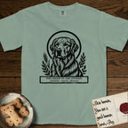 Holy Orders Golden Retriever T-Shirt flat lay in Bay, featuring a bold black-and-white linocut saint-medallion portrait of a Golden Retriever.