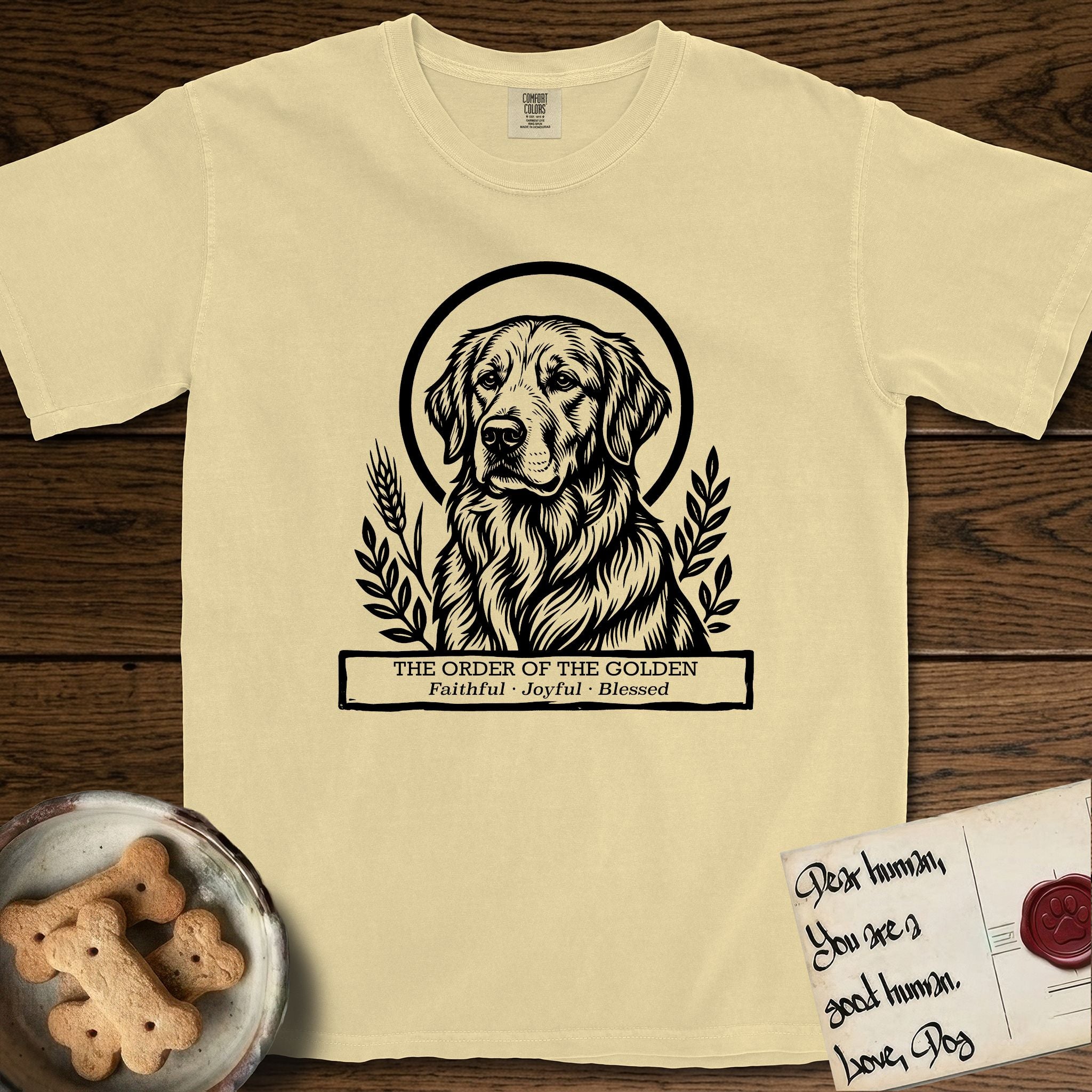 Holy Orders Golden Retriever T-Shirt flat lay in Butter, featuring a bold black-and-white linocut saint-medallion portrait of a Golden Retriever.