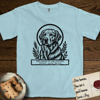 Holy Orders Golden Retriever T-Shirt flat lay in Chambray, featuring a bold black-and-white linocut saint-medallion portrait of a Golden Retriever.