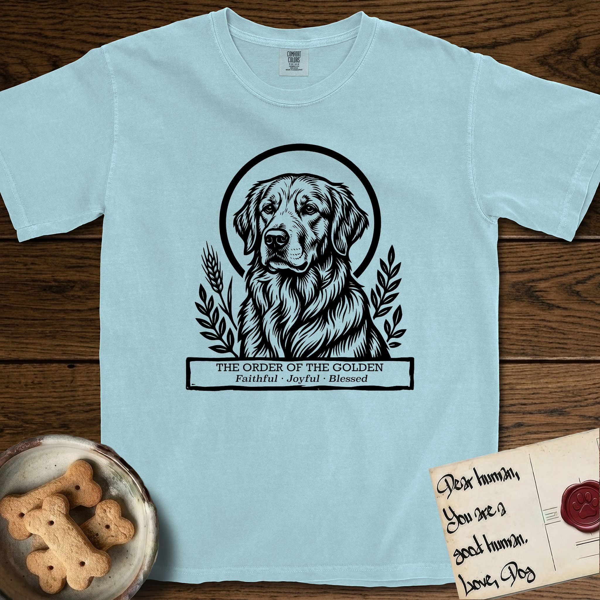 Holy Orders Golden Retriever T-Shirt flat lay in Chambray, featuring a bold black-and-white linocut saint-medallion portrait of a Golden Retriever.